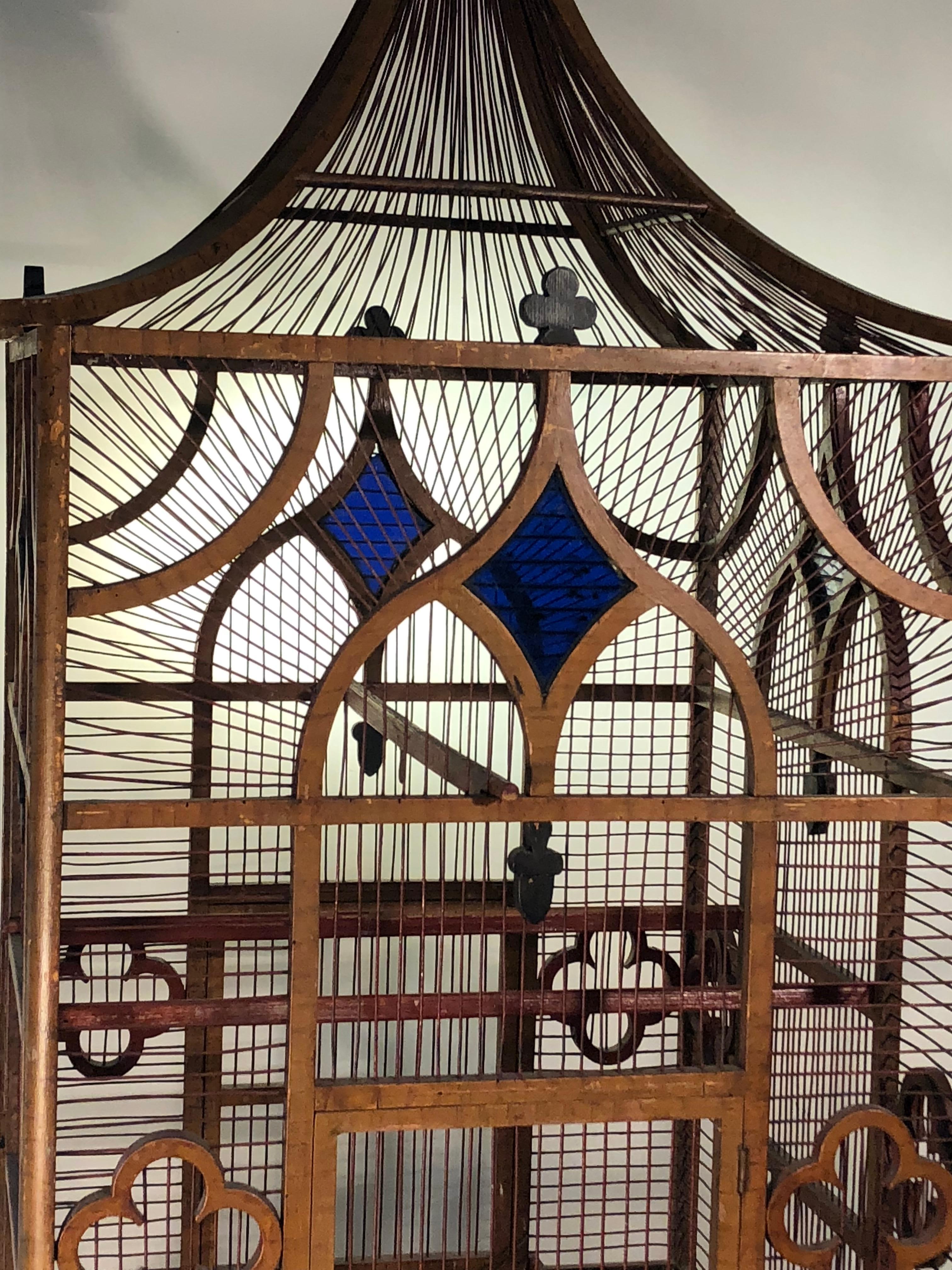 A large Pagoda-form faux-painted wood and wire birdcage, probably English, circa 1870 with carved and ebonized acorns and clovers and inset cobalt blue glass panes. The arched roof has a nicely turned wood finial. Original perches and feeder box.