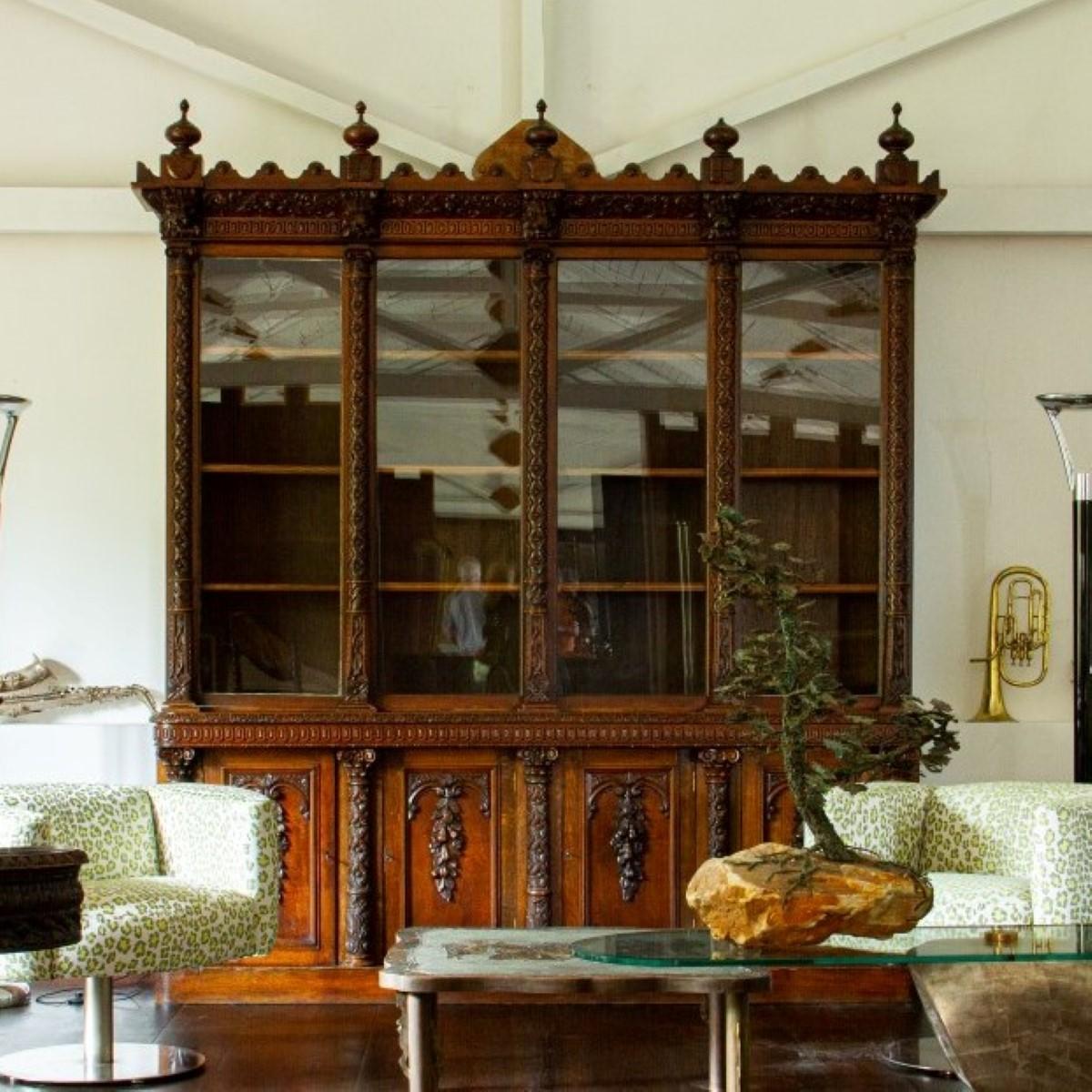 A monumental stained oak Victorian bookcase with five turned finials and lion masks adorning the pediment. The bookcase has four glazed doors, the middle of which are sliding doors. The doors are edged with heavily carved flowers on Corinthian style