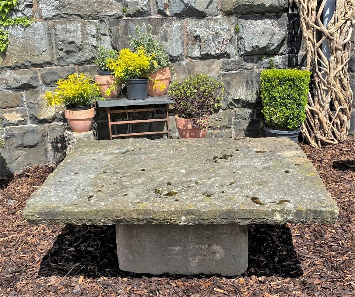 A large Victorian York Stone garden table. A huge single stone top measuring 5ft x 4ft sitting on a large sandstone plinth. Superbly weathered with a rough characterful natural surface. A low table which is also a good height for sitting on and