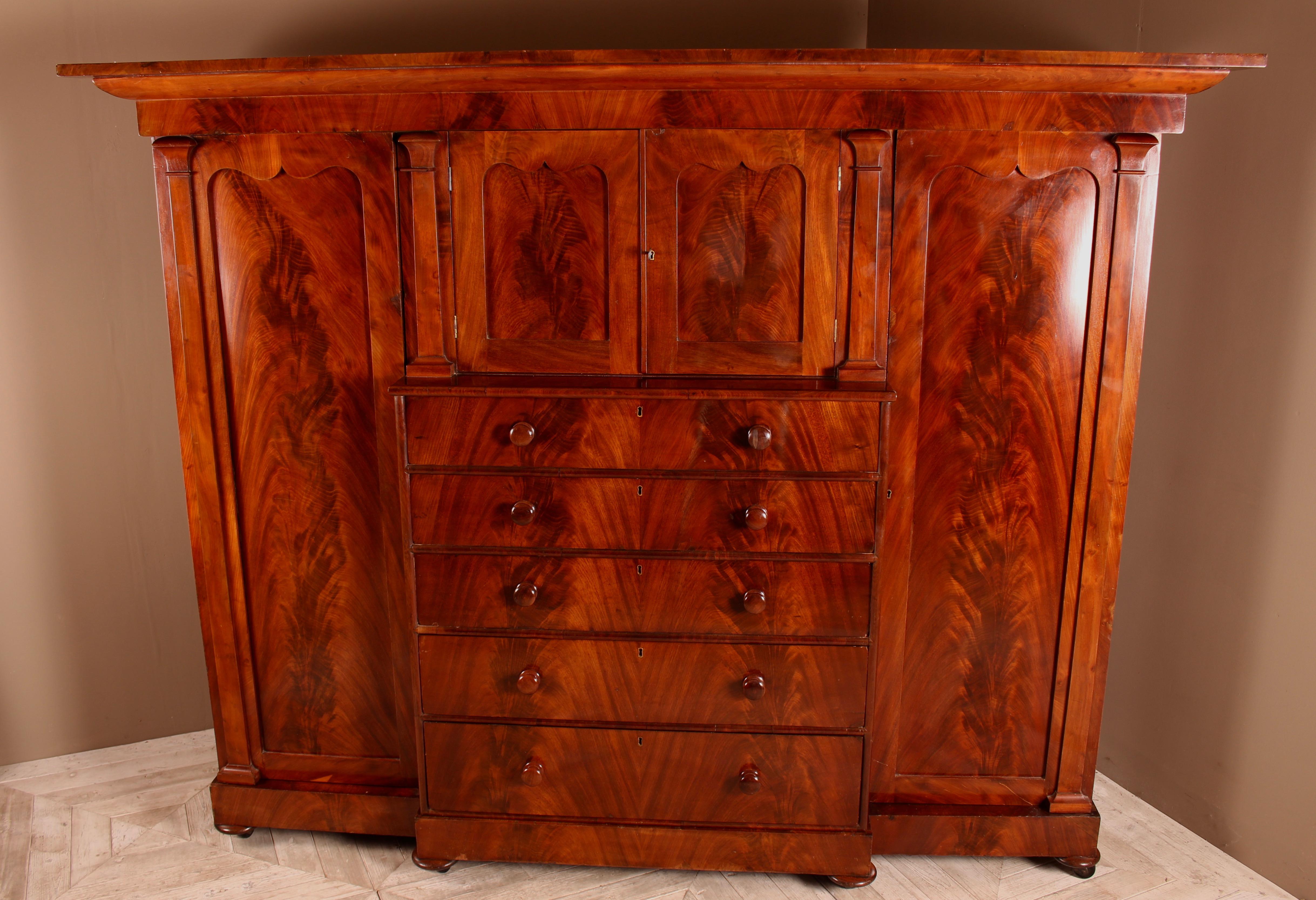 A handsome large Victorian flamed mahogany Compactum wardrobe of breakfront form. Having an attractive flared cushion pediment above a central shelved cupboard with five graduated drawers below. Flanked to either side with wardrobes with outer