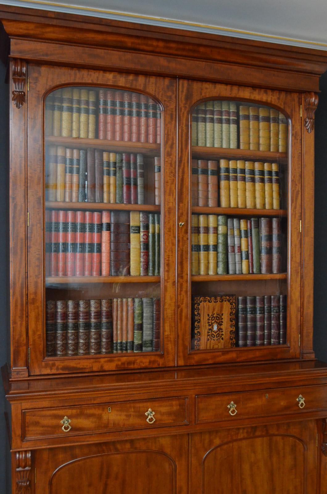 Moulded cornice above a pair of glazed doors enclosing 4 height adjustable shelves and flanked by drop carvings, projecting base with figured mahogany moulded drawers fitted with original brass handles, and a pair of panelled cupboard doors