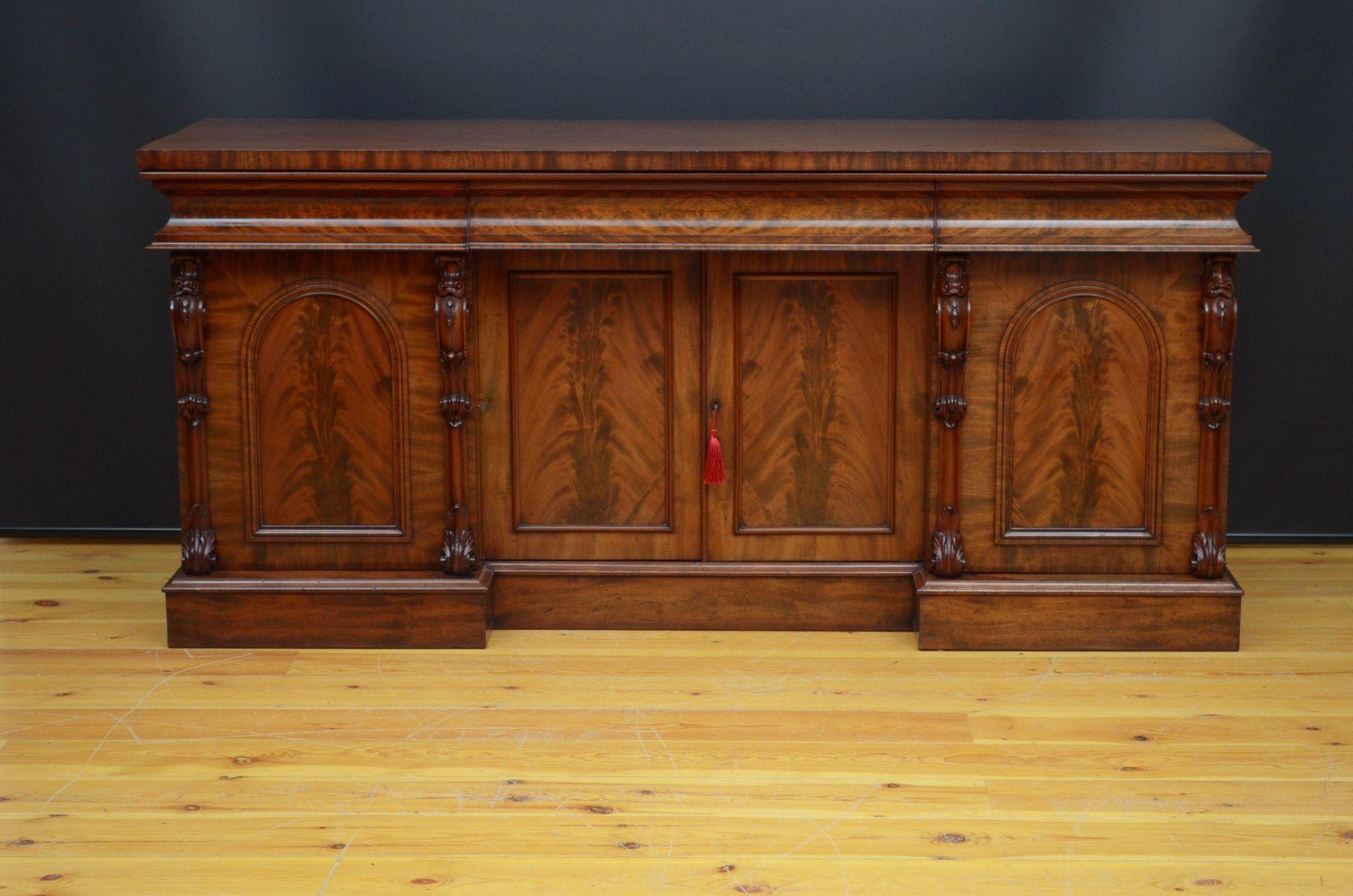 R025 Fine quality English Victorian sideboard in mahogany, having figured mahogany top above three concave shaped drawers and a pair of recessed, panelled, flamed mahogany cabinet doors fitted with original working lock and a key, all flanked by
