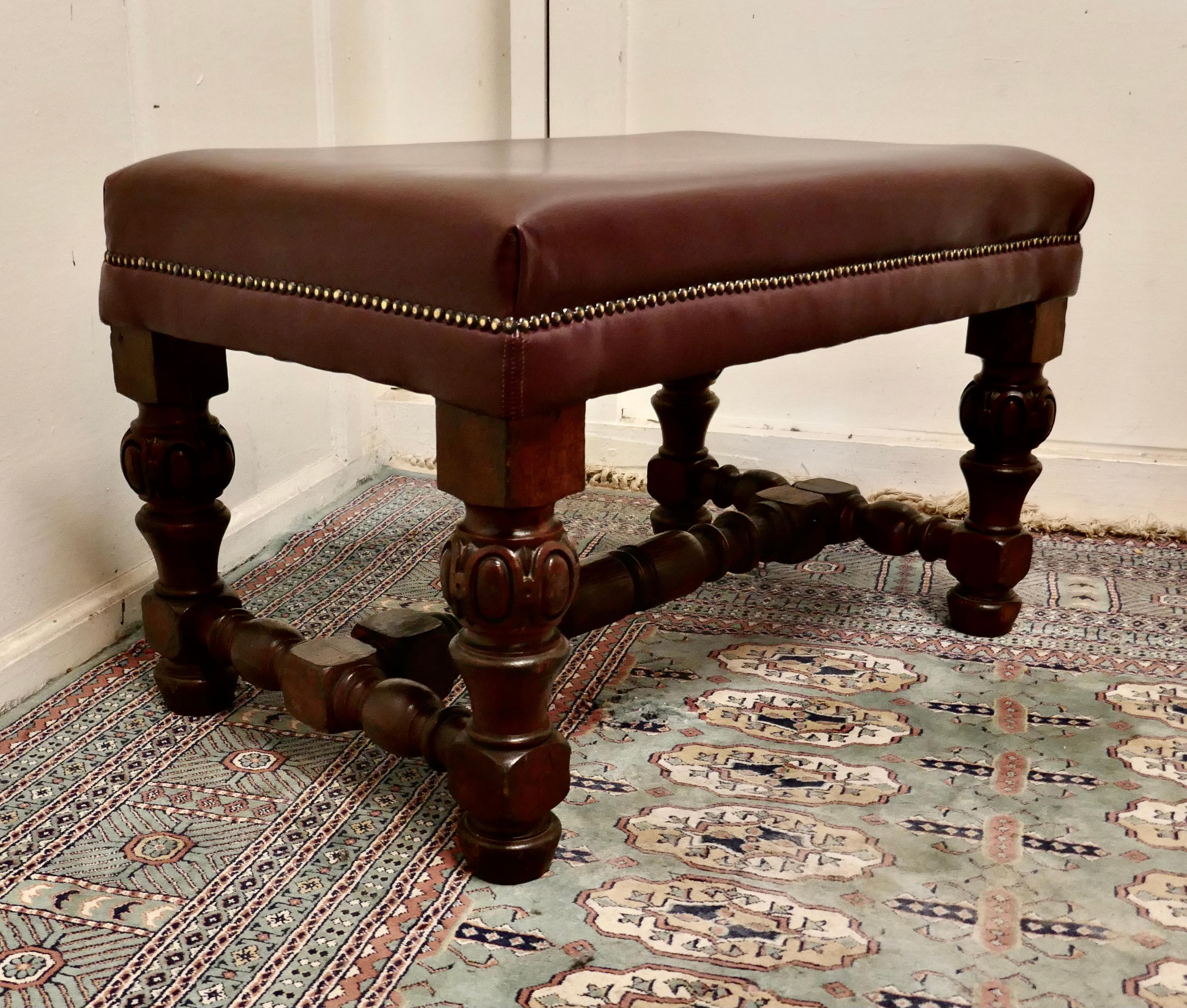 Large Victorian oak and leather library stool

The stool or window seat has chunky turned and carved legs with a turned cross stretcher 
The stool is upholstered in burgundy leather with brass studs 
This large sturdy library stool would work