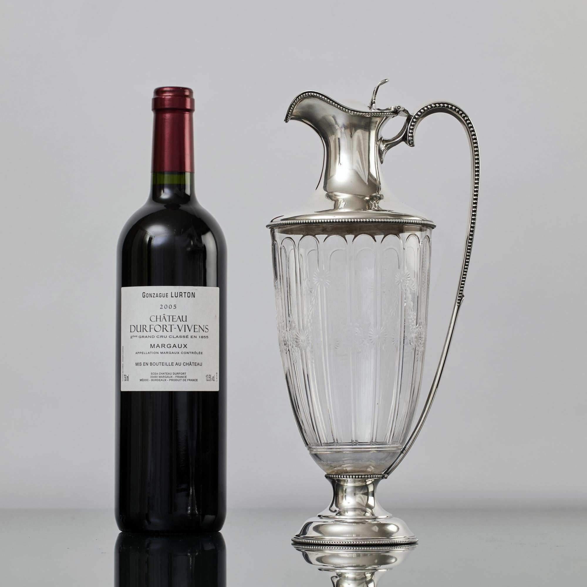 Elegant, neoclassical style engraved glass antique wine jug with silver handle and mounts. Made during the latter part of the Edwardian era, the jug's glass body is hand blow and beautifully hand engraved in floral swag patterns, typical motifs of