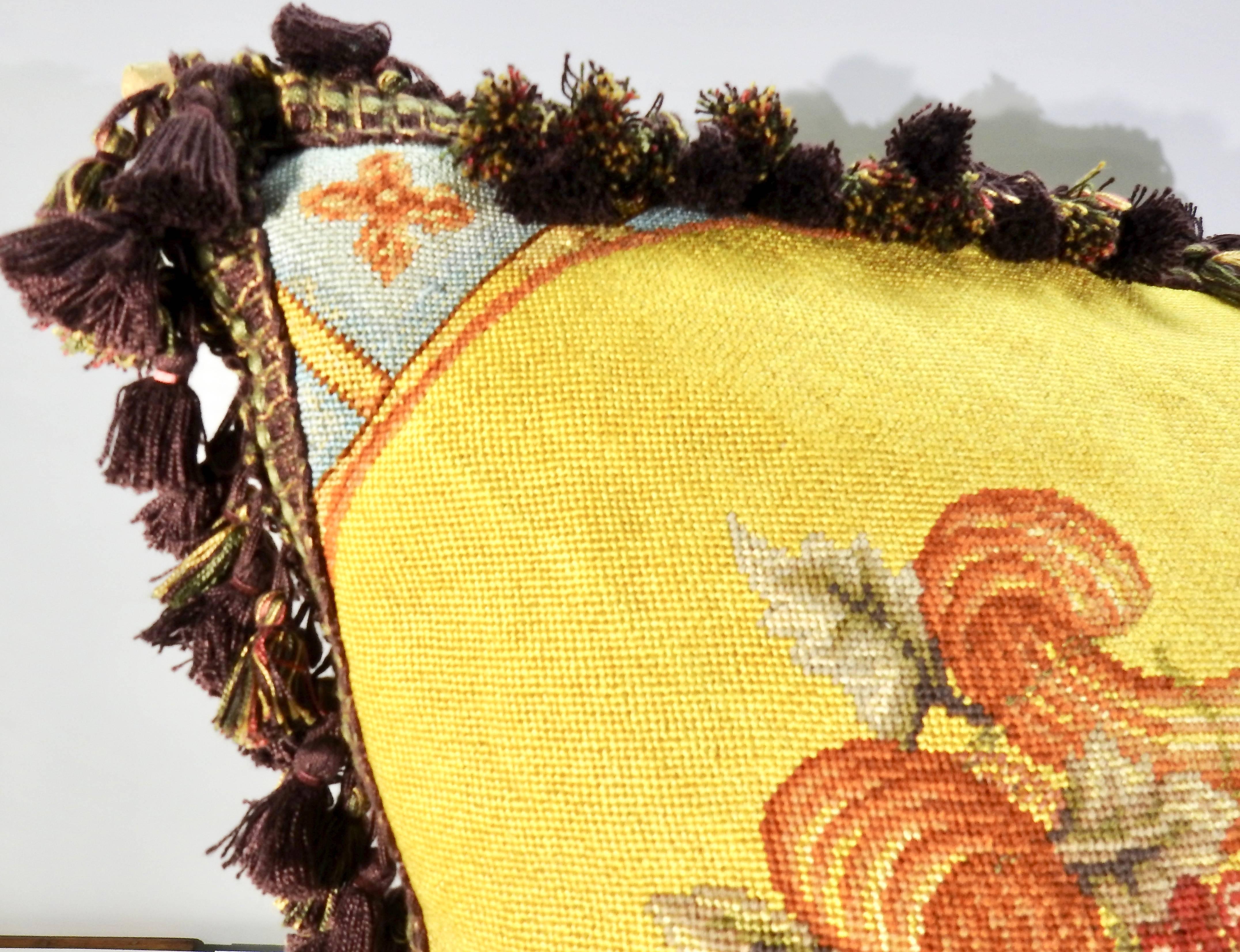 A fruit bowl takes center stage on this vintage needlepoint pillow with swirls of fruit surrounding it. The background is completed in a bold yellow with a variety of colors in the design. The back of the pillow is a soft, tan colored fabric with a
