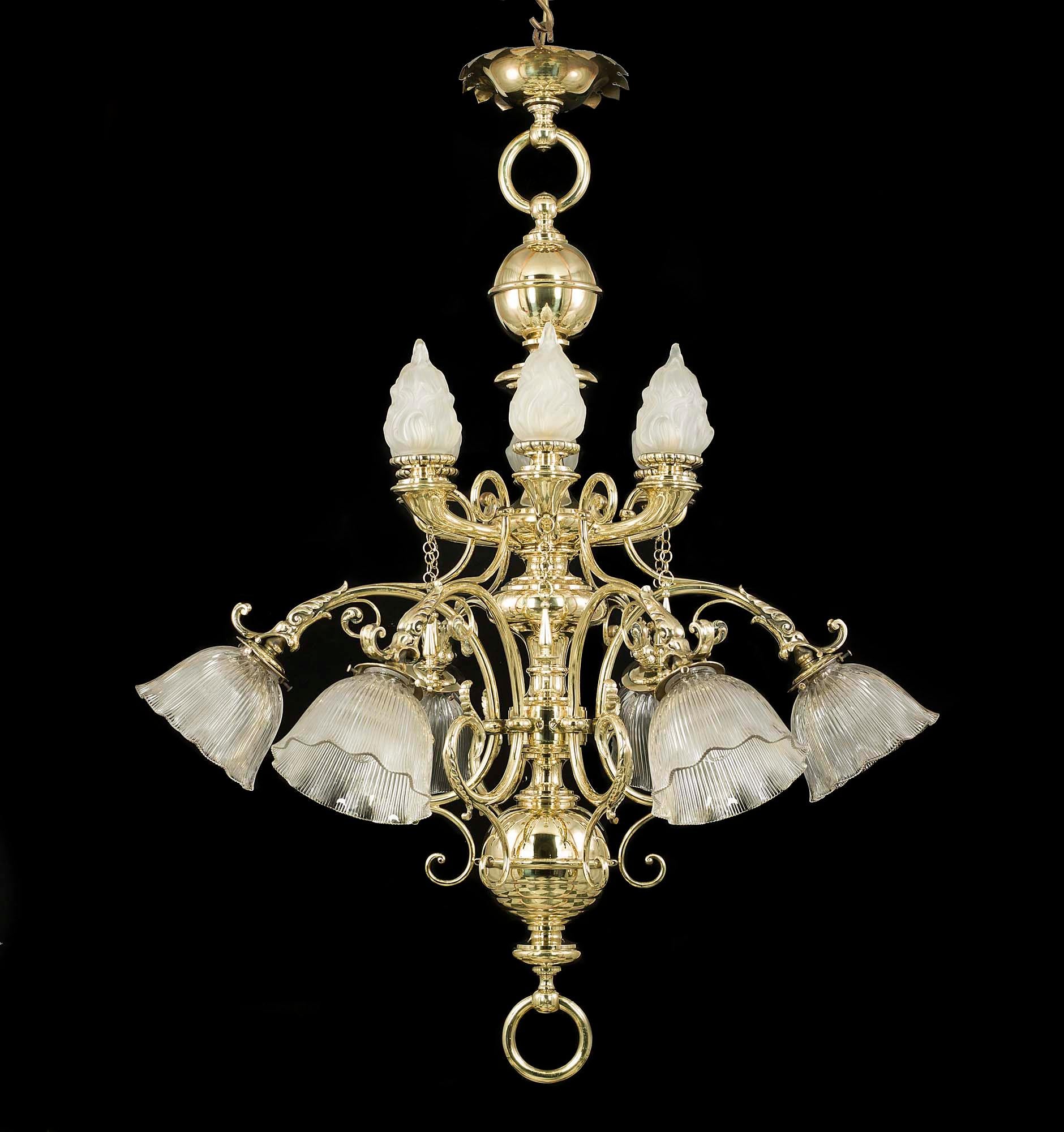 A large and magnificent late Victorian twelve-branch brass antique chandelier. Theatrical and grand the elaborate brass baluster stem has twelve scrolling arms issuing from two graduated tiers, the lights with six frosted glass flambeau shades above