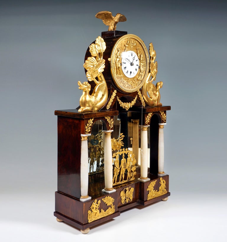 Splendid Viennese clock, ebonized fruitwood, with four alabaster columns in front of mirrored glass, above, flanking the cylindrical clock case, carved dolphins with new gilding, gilded pewter appliques, as well as a removable gilded pewter front