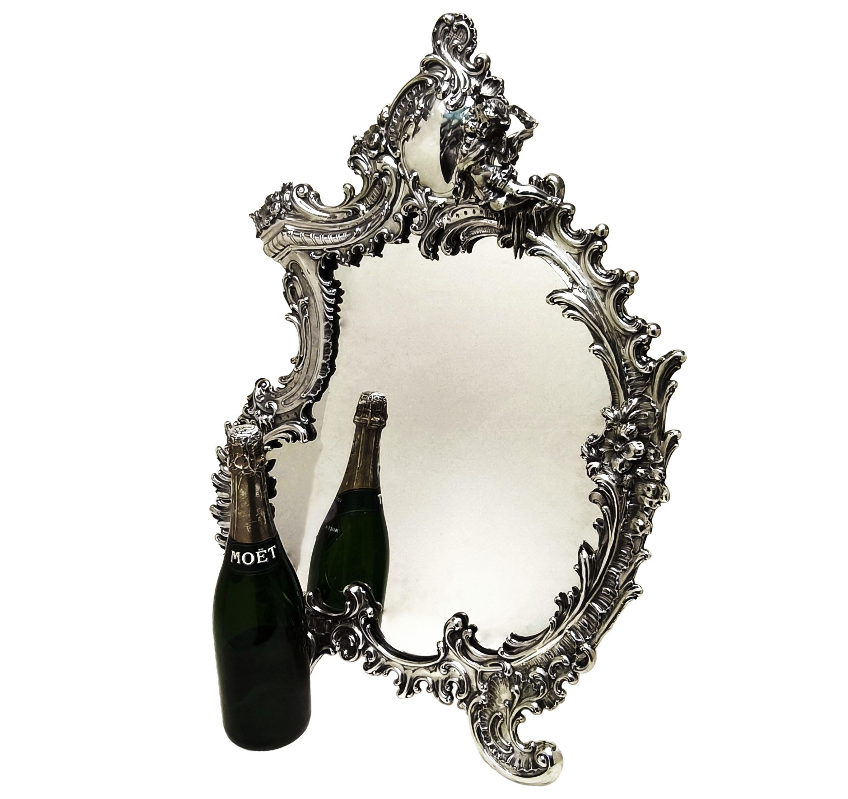 A magnificent Antique Silver Table Mirror with classic Rococo style designs. This Large Antique Mirror has an elegantly asymmetrical shape and an ornate border of scrolls, flowers and subtle architectural details. The Top Border of the mirror has a