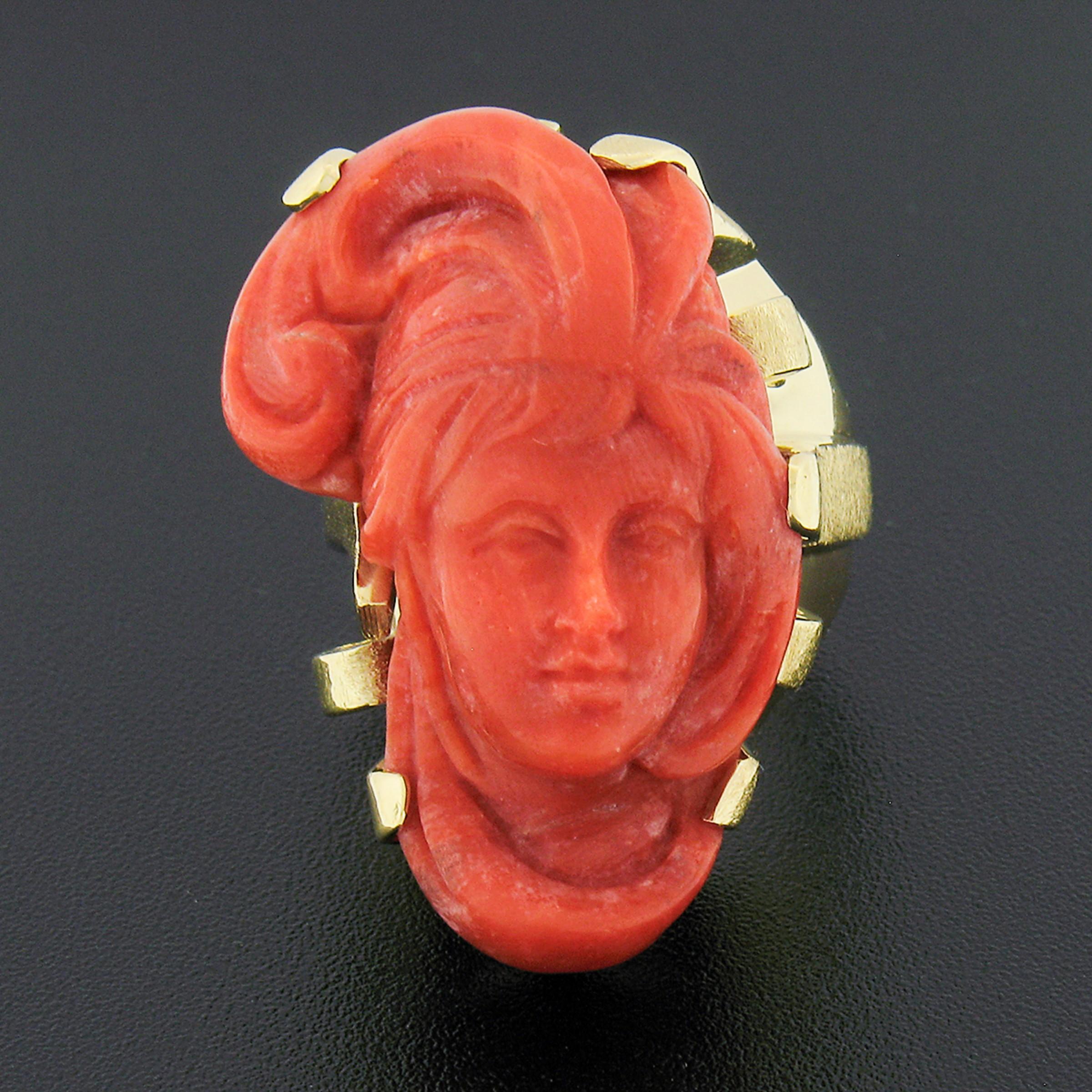 This large, unique, and very well-made vintage ring was crafted from solid 14k yellow gold and features a GIA certified natural coral neatly set at the top. The large coral is a reddish-orange color and is masterfully carved into a portrait of a