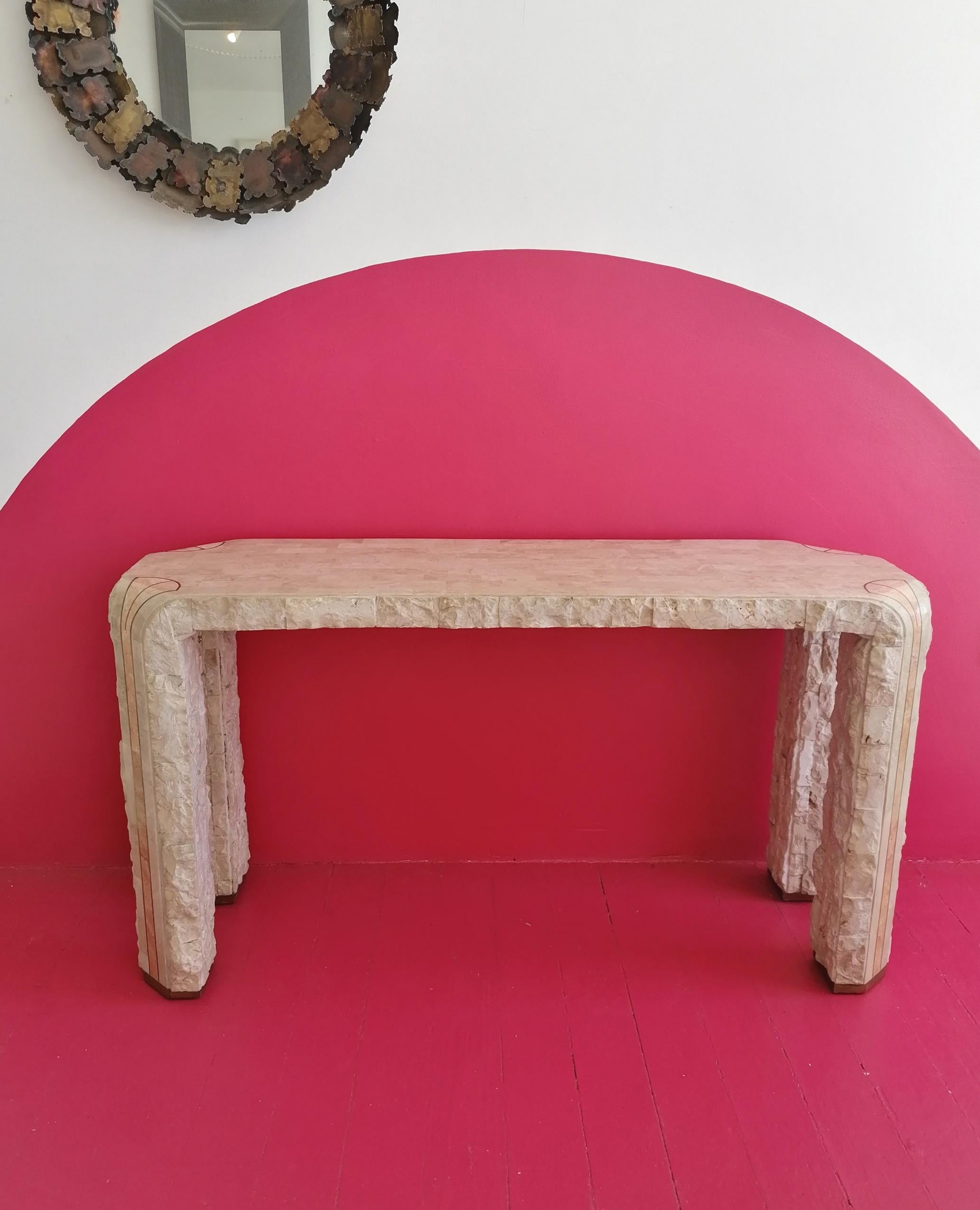 Large postmodern Maitland Smith console table: polished tessellated stone with rough-hewn edges. Corners have a pink-toned stone detail with brass inlay. Brass-trimmed legs. USA, 1980s.