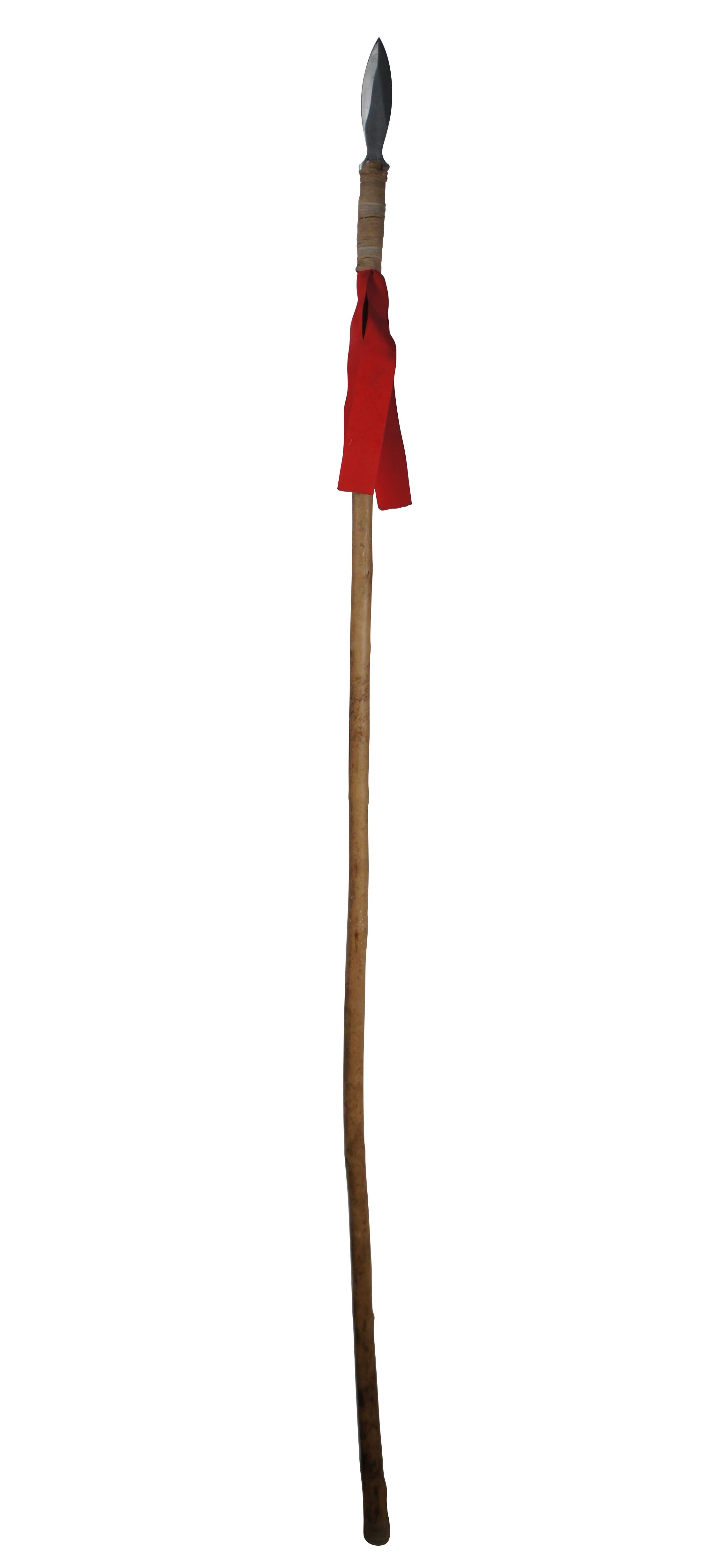 Late 20th century 6 foot long Javelin spear. 440 Stainless steel leaf shaped tip on a natural wood branch wrapped with leather cord and decorated with red grosgrain ribbons.

Dimensions:
1.5