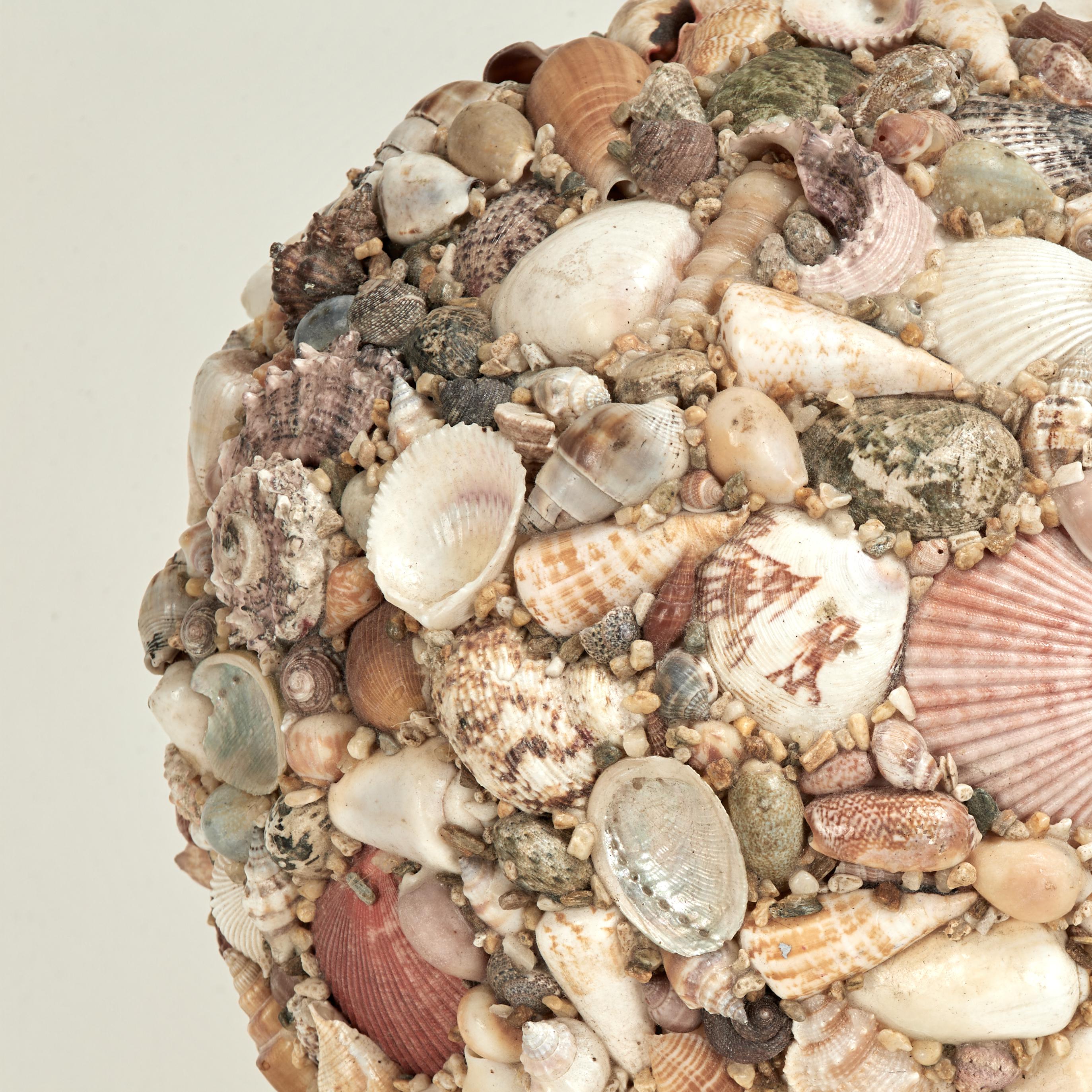A large and lofty mid century ocean inspired sphere ambitiously handcrafted in an eccentric composition of exotic seashells and presented on an ebonized wood base. 