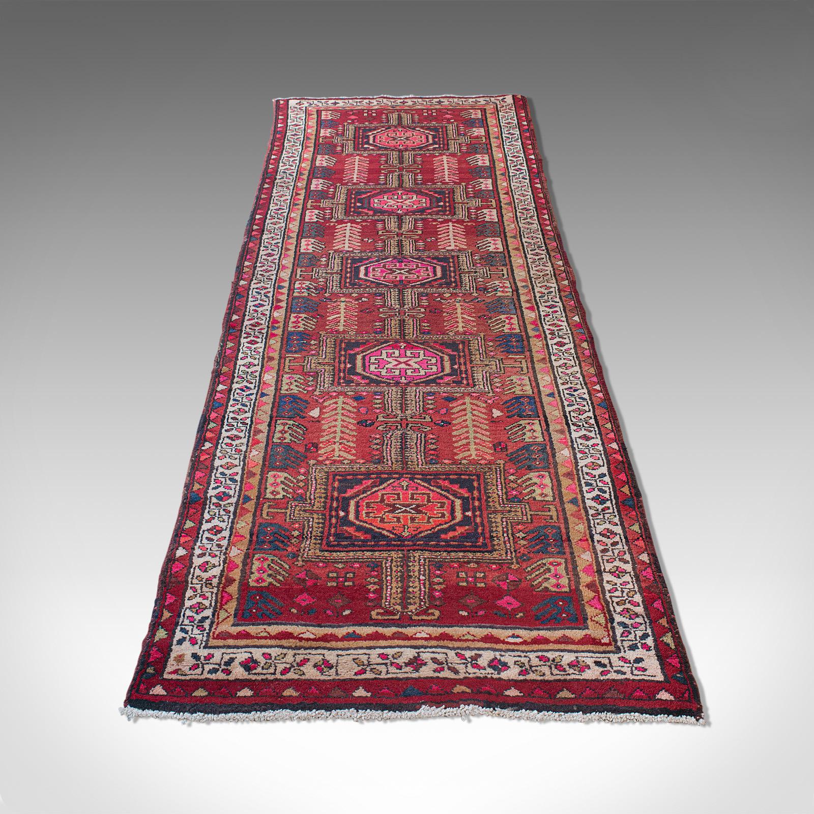 This is a large vintage Baluchi hallway runner. A Persian, woven hall rug or carpet, dating to the mid-20th century, circa 1960.

Dashing colors and great length for the grand reception hall
Displaying a desirable aged patina
Woven crimson