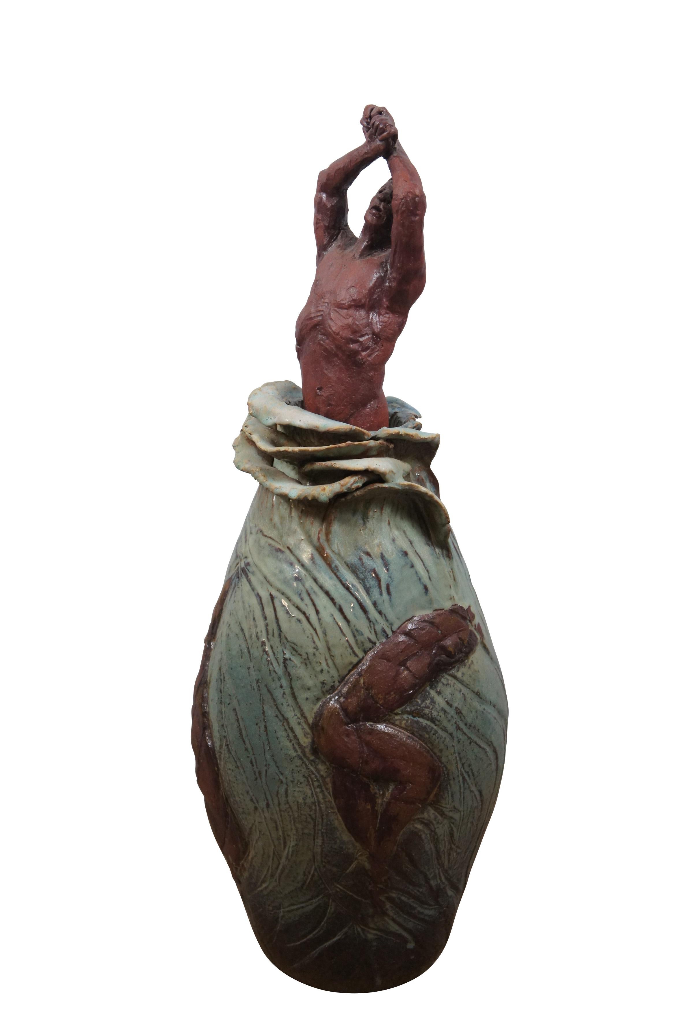 Vintage ceramic art sculpture by Bob Coates. Features a male figure emerging from the waist up from a swirling green base that resembles ocean waves or a veined flower bud, decorated with other brown figures in various dancing / falling attitudes.