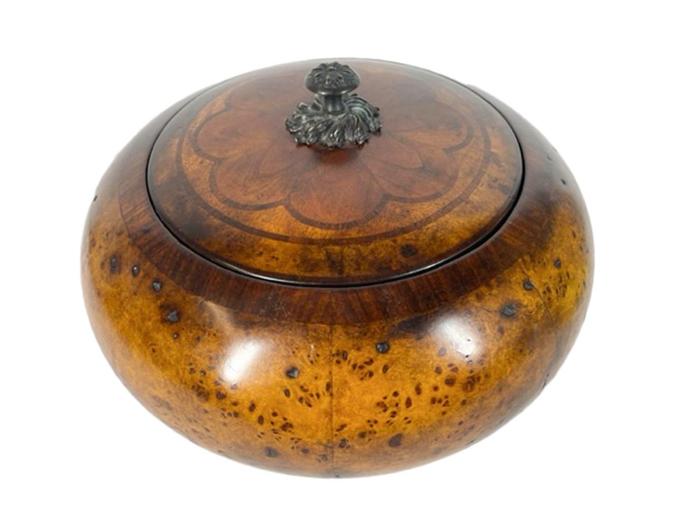 Large turned wood box or covered bowl of compressed ball form. The body covered in wide segments of burled walnut veneer with crossbanding at the opening, the cover with lobed panels within a circle and with a crossbanded edge all centering a cast