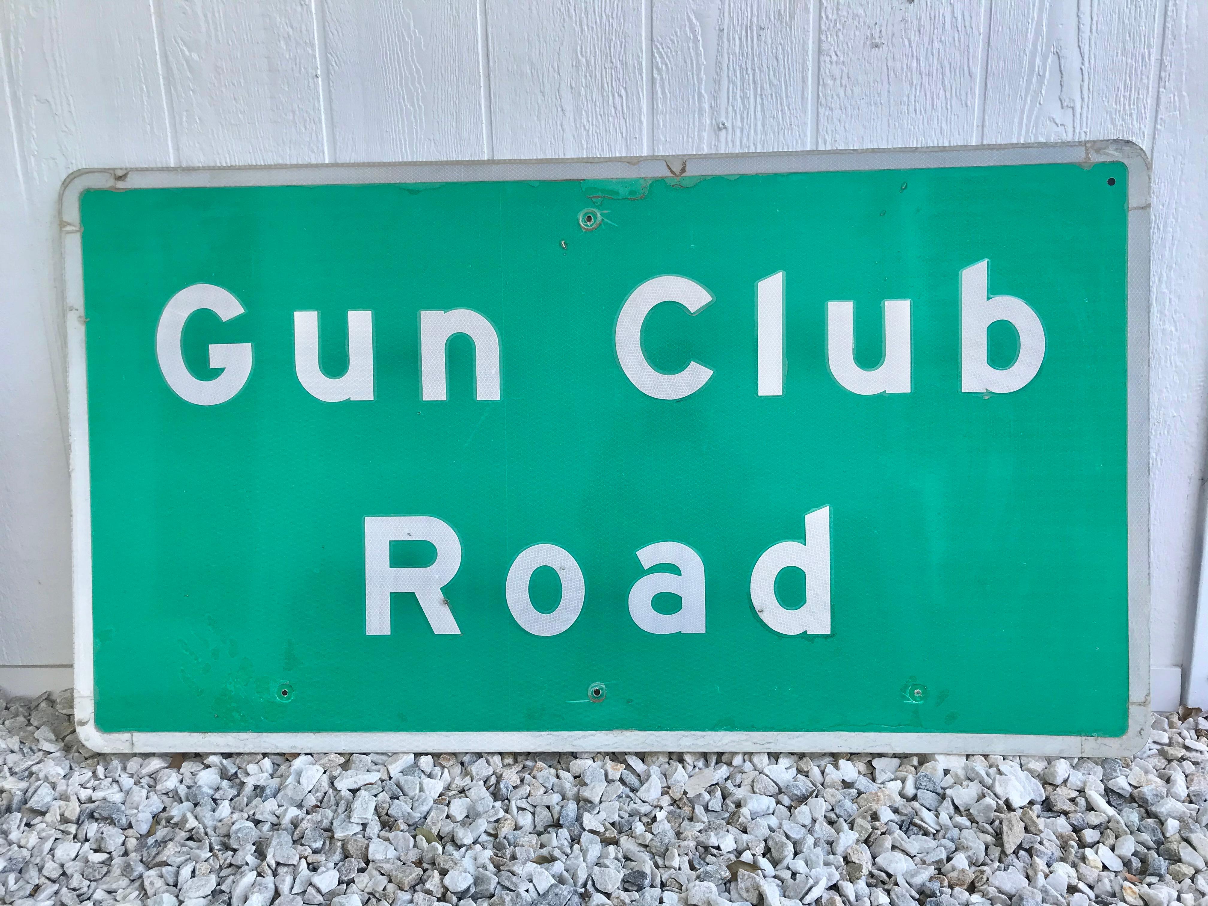 Ein altes Straßenschild aus Stahl mit der Aufschrift Gun Club Road. Sign wurde in der Wüste in Kalifornien, nördlich von Bakersfield, pensioniert. Grünes, reflektierendes Schild mit weißer Beschriftung und Verzierung. Guter alter Zustand. Einige