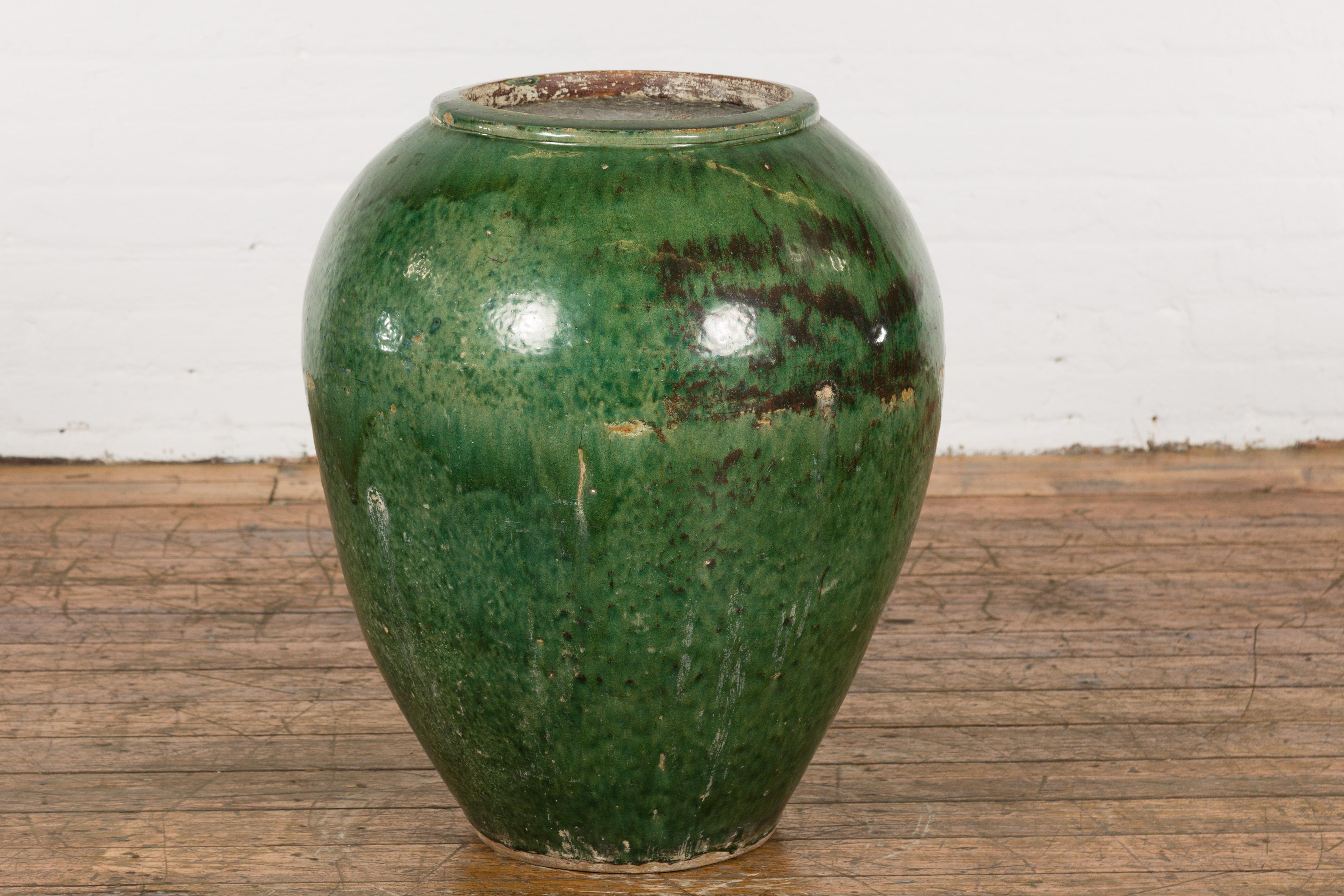 A large vintage Chinese green glazed vessel with brown accents, tapering lines and weathered appearance, perfect to be used as a garden planter. Invigorate your outdoor space with this large vintage Chinese green glazed vessel, an piece echoing the