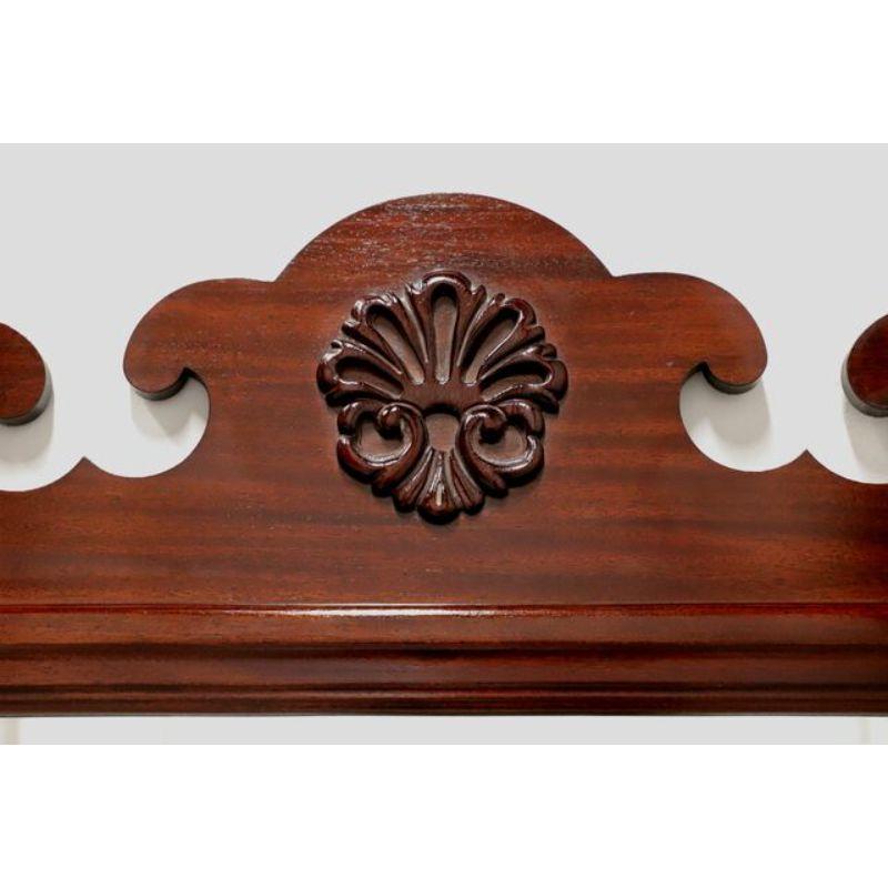 A large Chippendale style wall mirror, unbranded, similar quality to Drexel or Henkel Harris. Bevel edge mirrored glass, mahogany frame with decorative carving to top and bottom with top center fleur-de-lis. Made in the USA in the late 20th