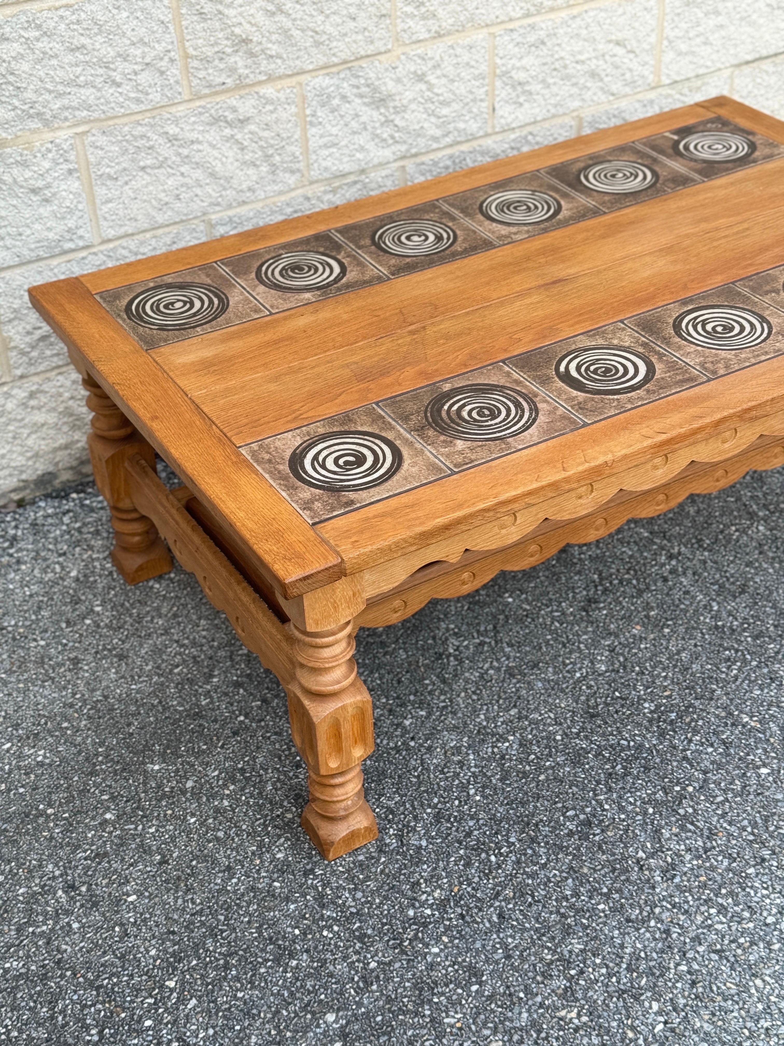 Vintage Danish piece made of oak, featuring chunky carved legs and a tile top. The tiles showcase a swirl design and are marked 