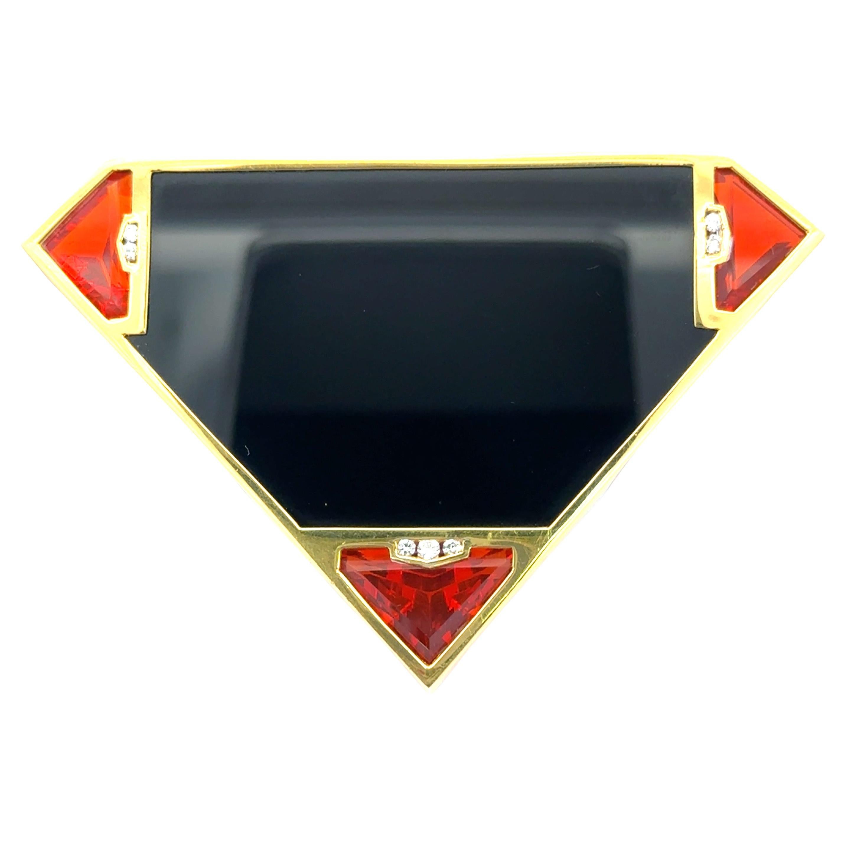 A bold and modern statement piece, this exquisite brooch is crafted in 18kt yellow gold, featuring a geometric trapezoid design inspired by Art Deco elegance. The centerpiece is a polished black onyx stone, framed by vivid trillion-cut garnets at