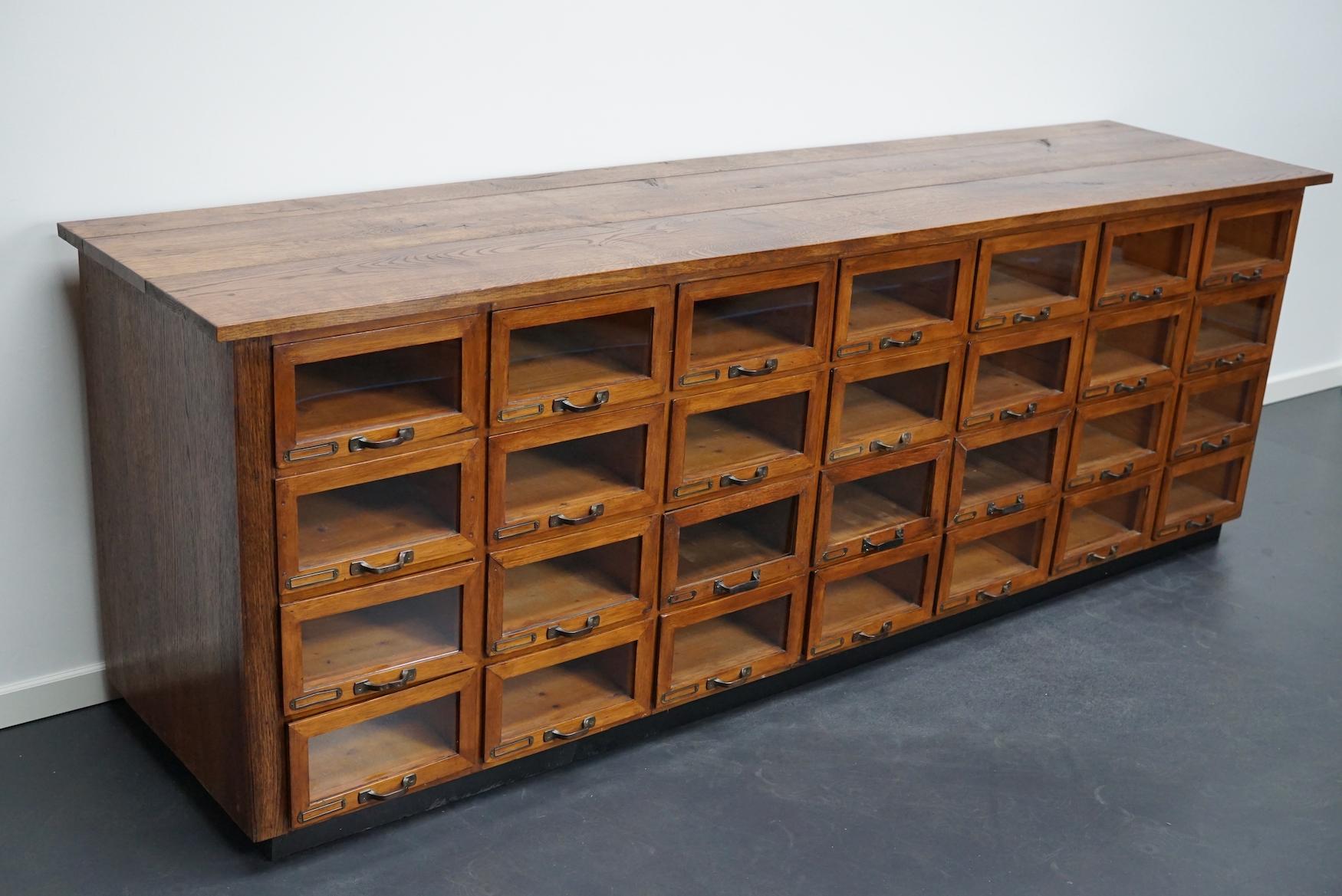 This haberdashery cabinet was produced during the 1930s in the Netherlands. This piece features 28 drawers with ply oak / glass fronts and brass hardware. It was originally used in a shop for sewing supplies and fabrics in Amsterdam. The interior