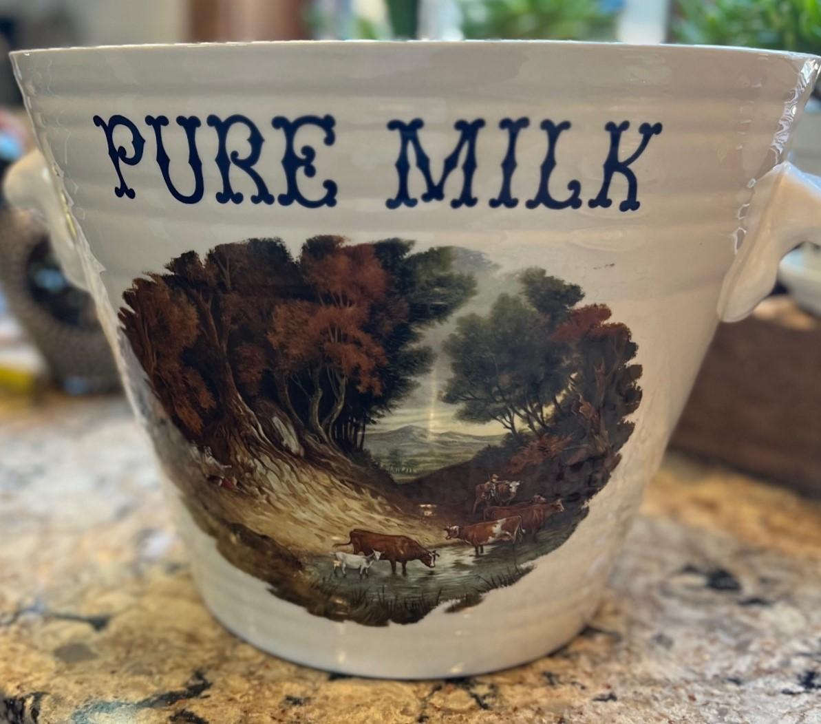 A vintage two-handled Edwardian style ironstone pottery milk pail printed with the words 'Pure Milk' in navy above a transferware graphic of a bucolic English scene. It has a banded design to the ironstone with nicely molded handles applied to each