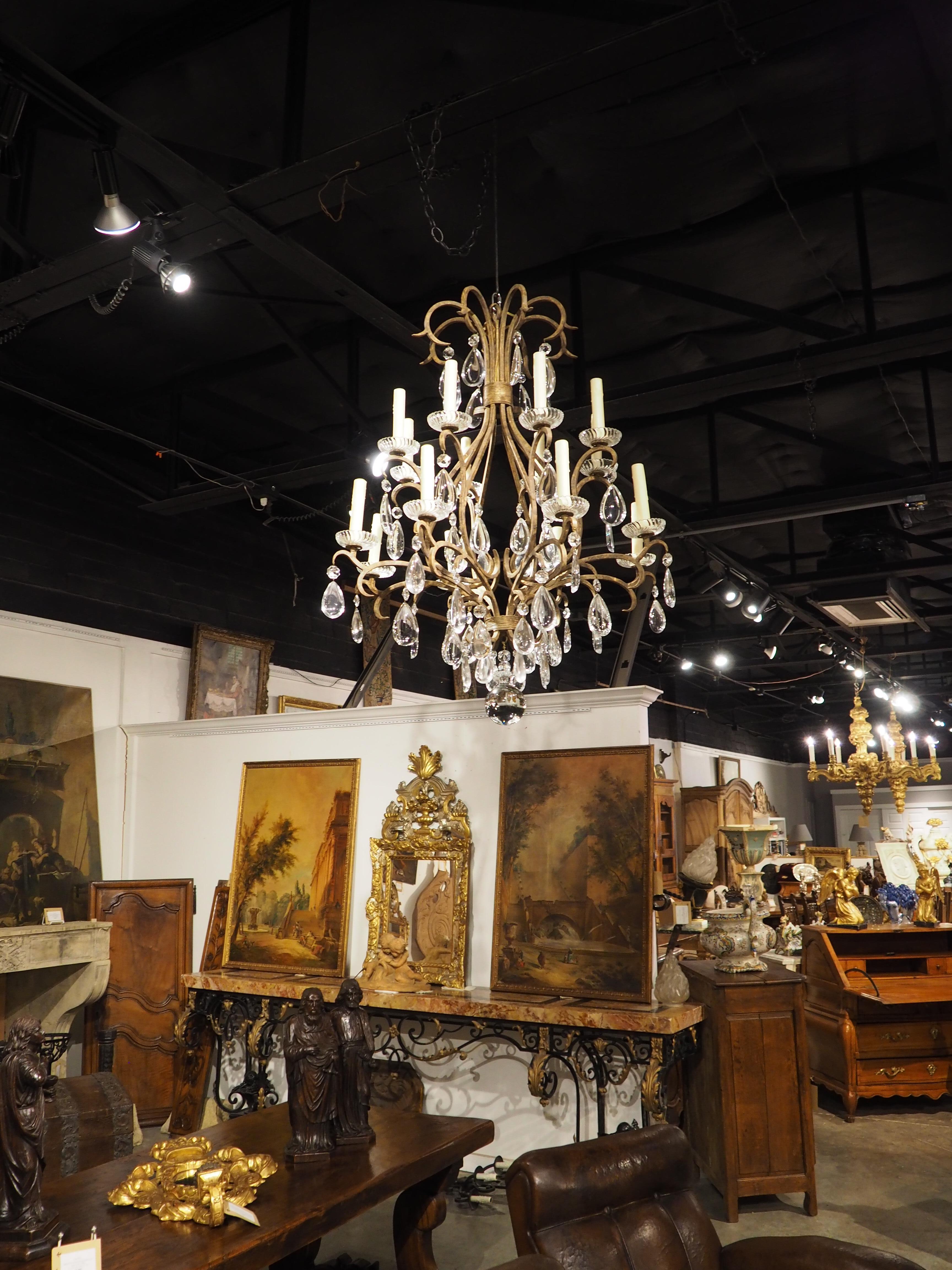 A beautiful wrought iron and crystal candelabrum dating to the late 1900s, this large French chandelier has an elaborate display of scrolled iron interspersed with teardrop crystal pendeloques. The main body is comprised of eight convex curved bars