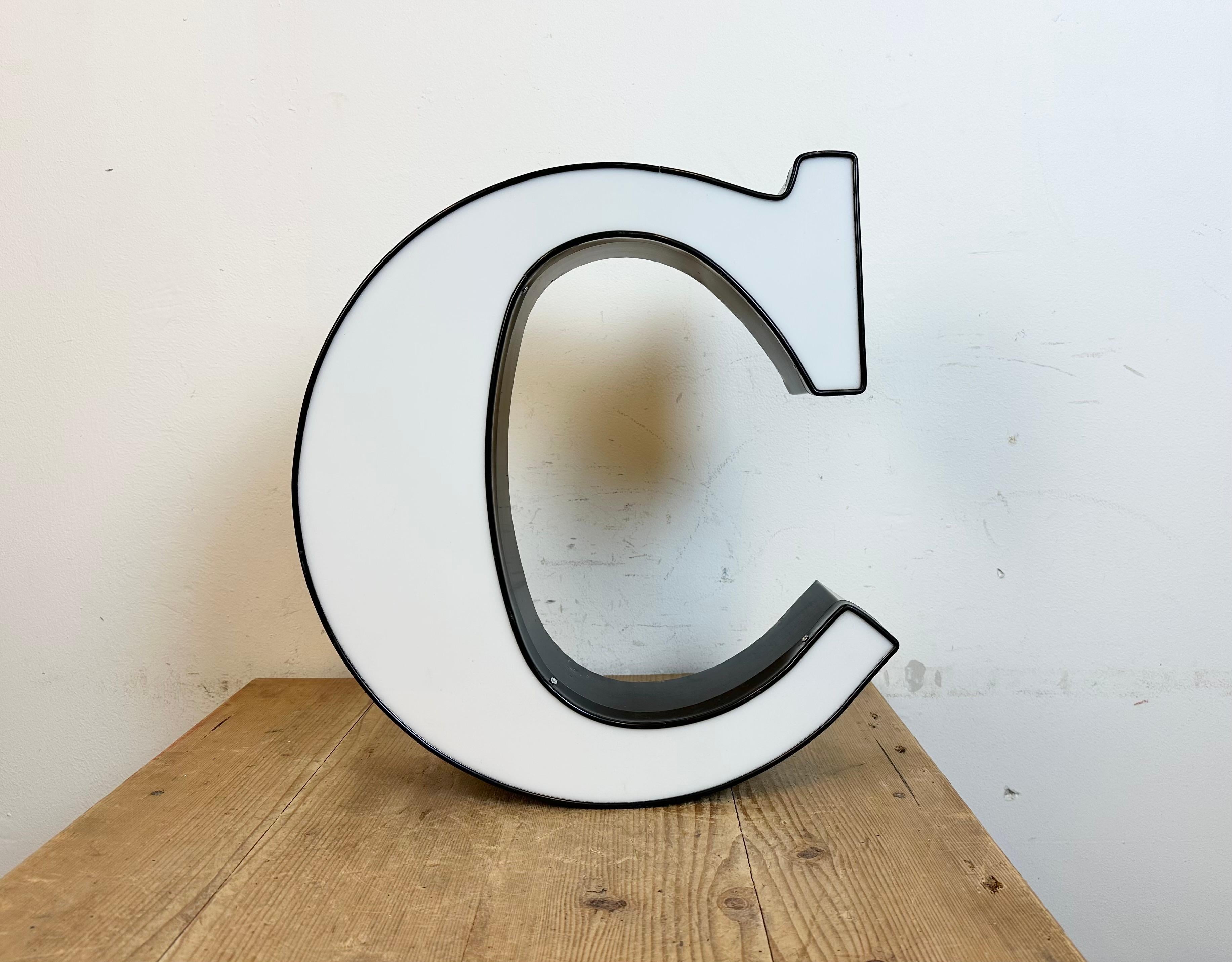 This vintage industrial illuminated letter C was made in Italy during the 1970s and comes from an old advertising banner. It features a black metal body and a white plexiglass cover. It is equipped with a LED strip. The letter can be used as a table