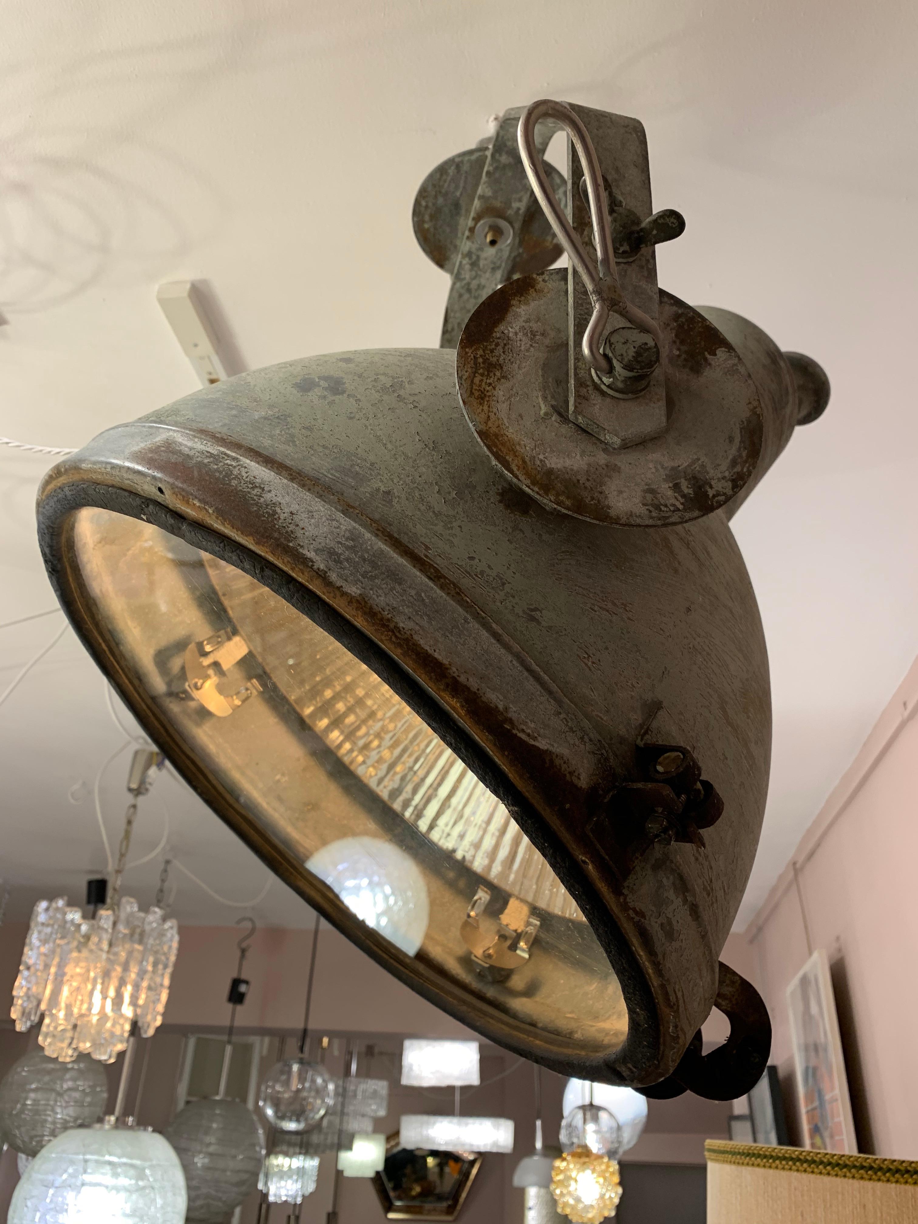 A large vintage industrial hanging factory lamp. The light hangs from a brass hook and swivels according to where you would like the light to be directed. The lamp has a beautiful aged patina and a matt grey/green finish. The single E27 screw in