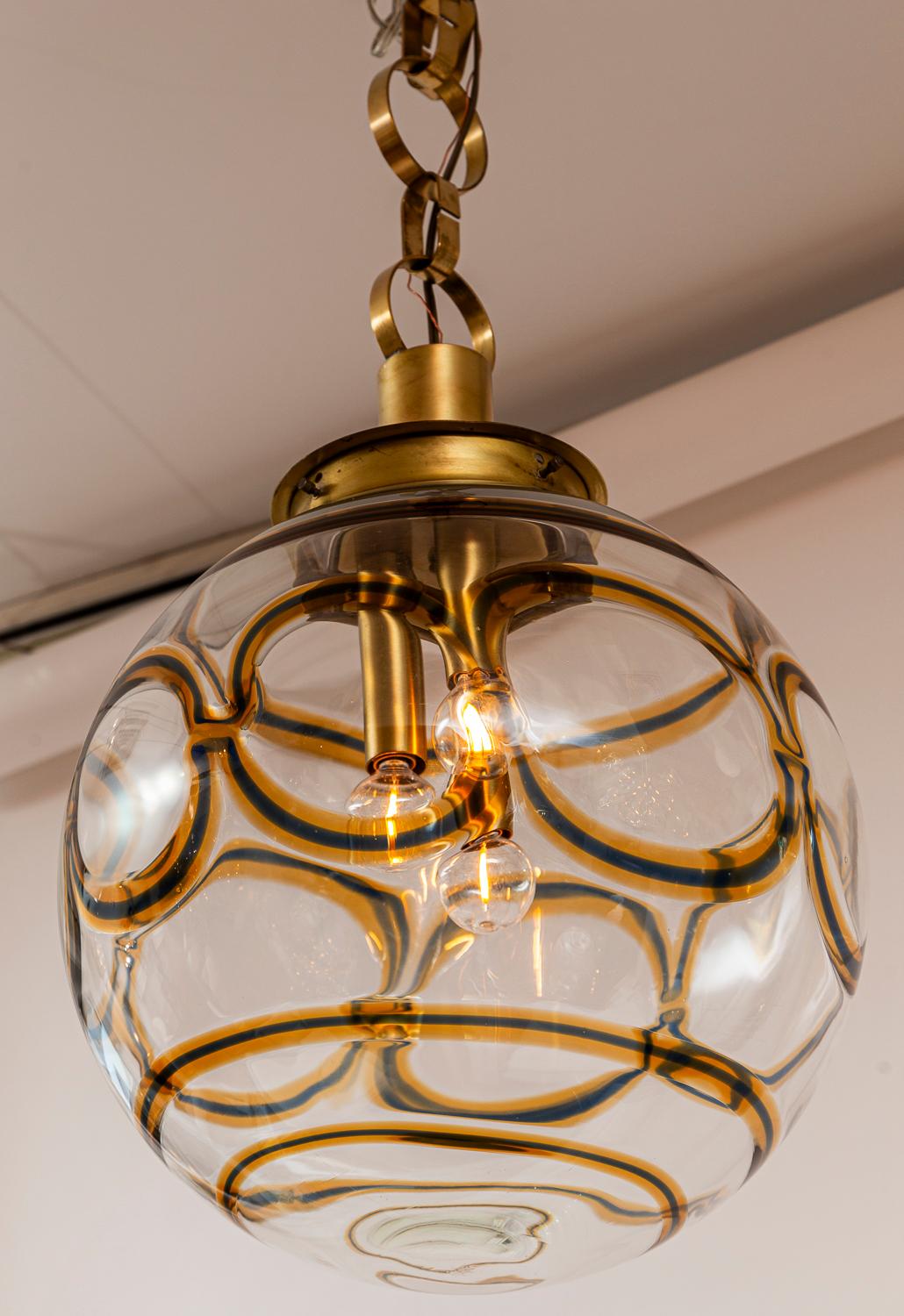Meraviglioso  e unica plafoniera a forma di globo soffiato trasparente con audaci colori ambra e  con tre candelabri sfalsati e con la catena originale in ottone.

Origine: Murano, Italia

Designer: Attribuito a AV One Mazzega

Datazione: