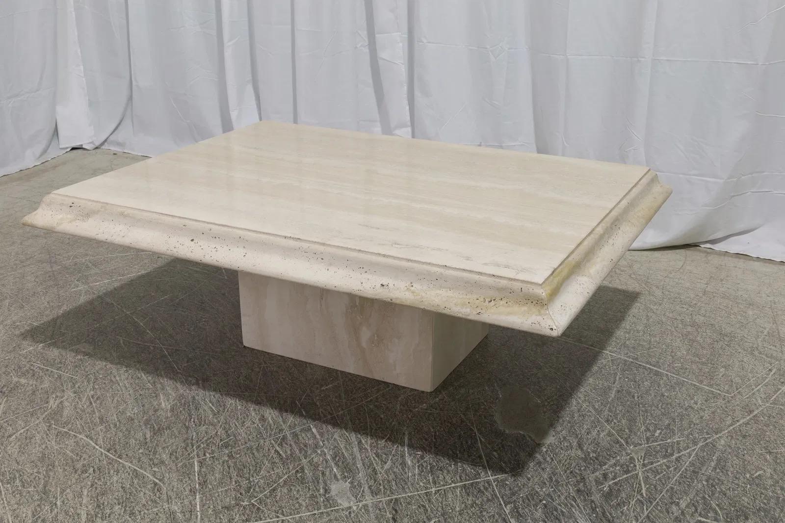 Table basse italienne en travertin, construite en deux parties, avec un plateau rectangulaire et une base solide. Le travertin présente des veines naturelles et des tons chauds. 