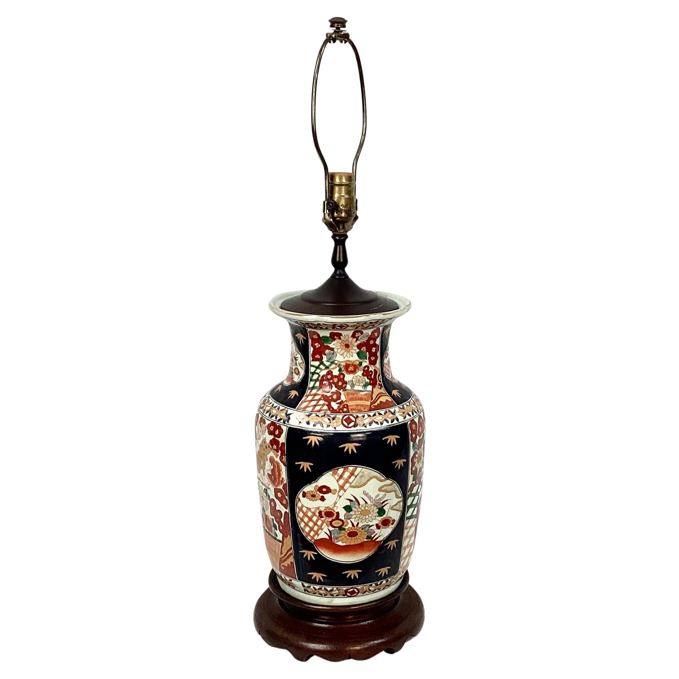 Early 20th century Japanese Imari vase porcelain lamp. Features beautiful cobalt blue with red, orange and white hand painted floral design, and gold trim. Lamp sits on a sturdy dark brown wooden vase. Harp and finial included. The height of 29