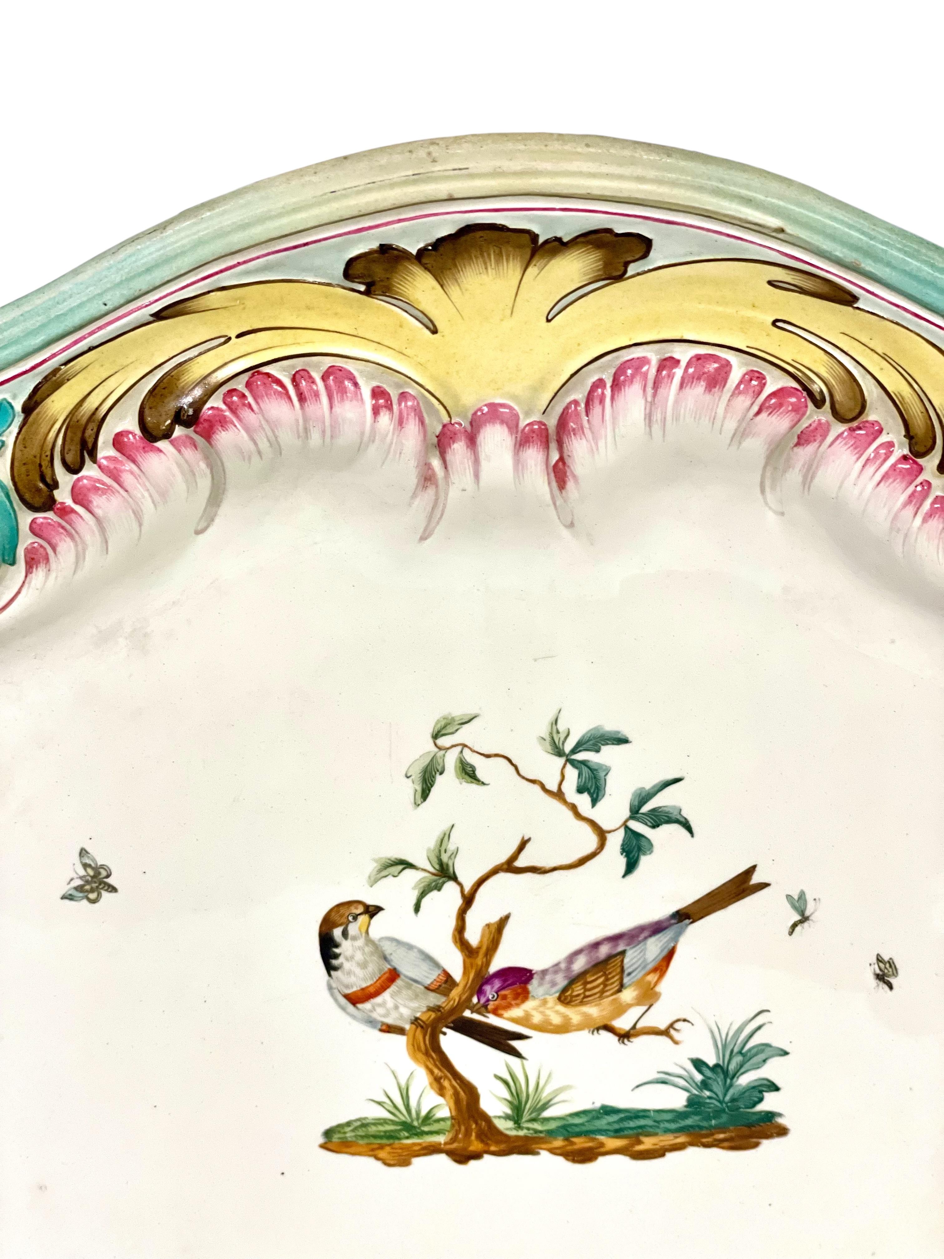 This large and very striking antique Majolica serving platter, roughly oval in shape, is hand- painted with an exceptionally fine central motif of exotic birds perched atop a tree, encircled by tiny butterflies. The border is exuberantly decorated