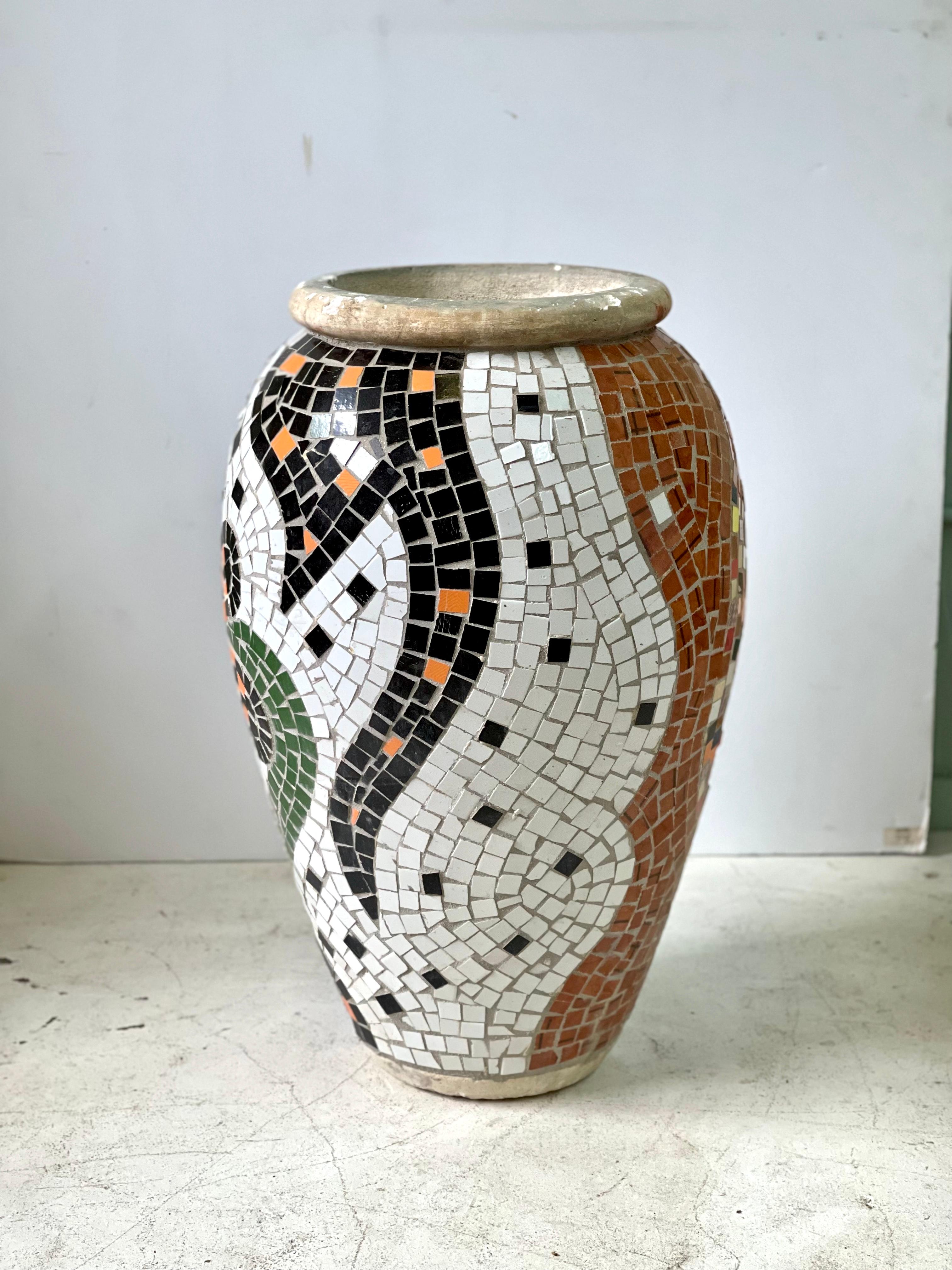 This is a wonderful 20th Century large mosaic urn-shaped planter from the Mediterranean region. It is handcrafted from ceramic tiles set into concrete having a black and white floral design on one side and polychrome tiles weaving through terracotta