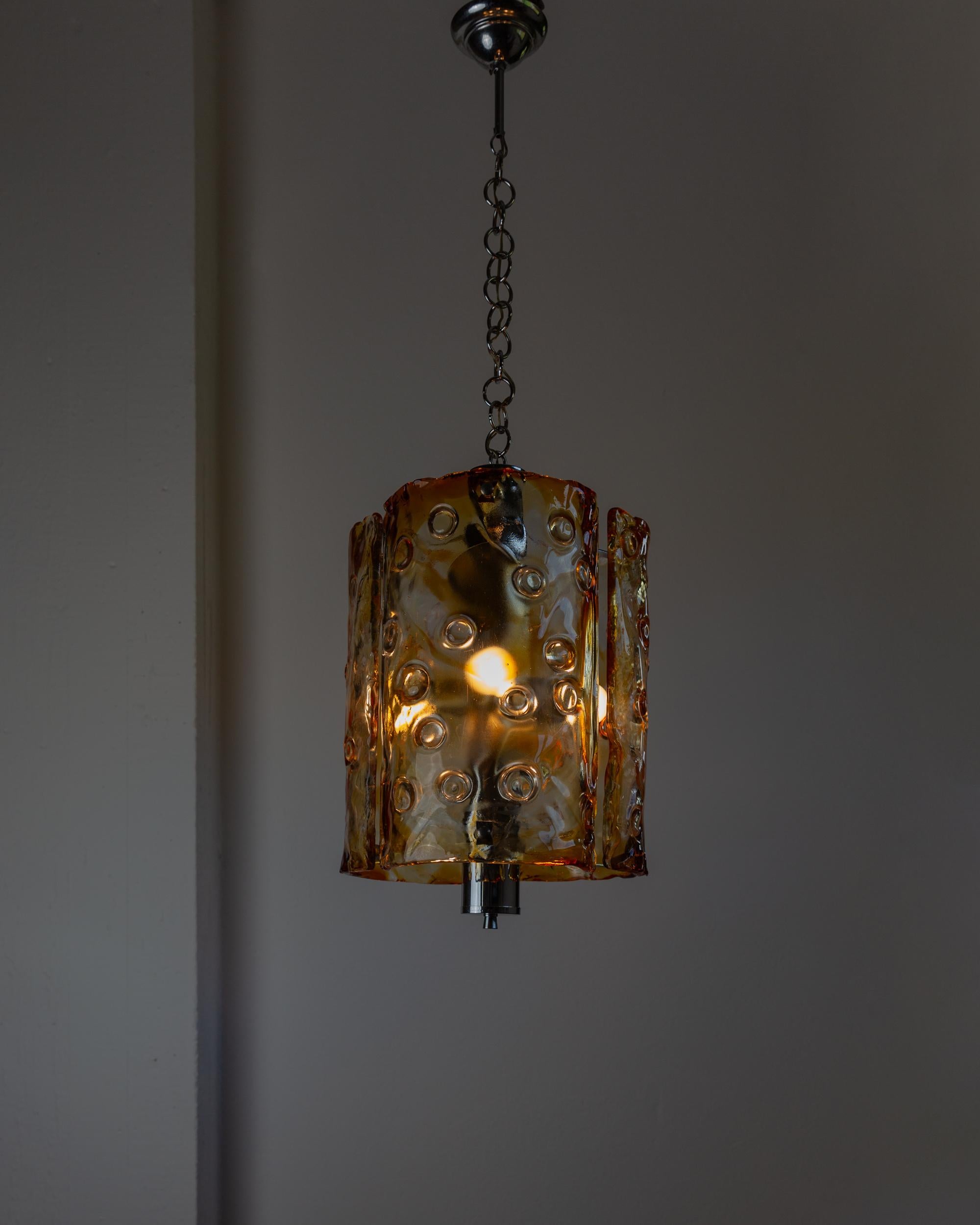 Questa imponente lampada da soffitto vintage in vetro di Murano di Toni Zuccheri per Mazzega, risalente agli anni '70, unisce eleganza e design contemporaneo. Con vetri chiari e ambrati e un elemento cromato, questo lampadario è un vero e proprio