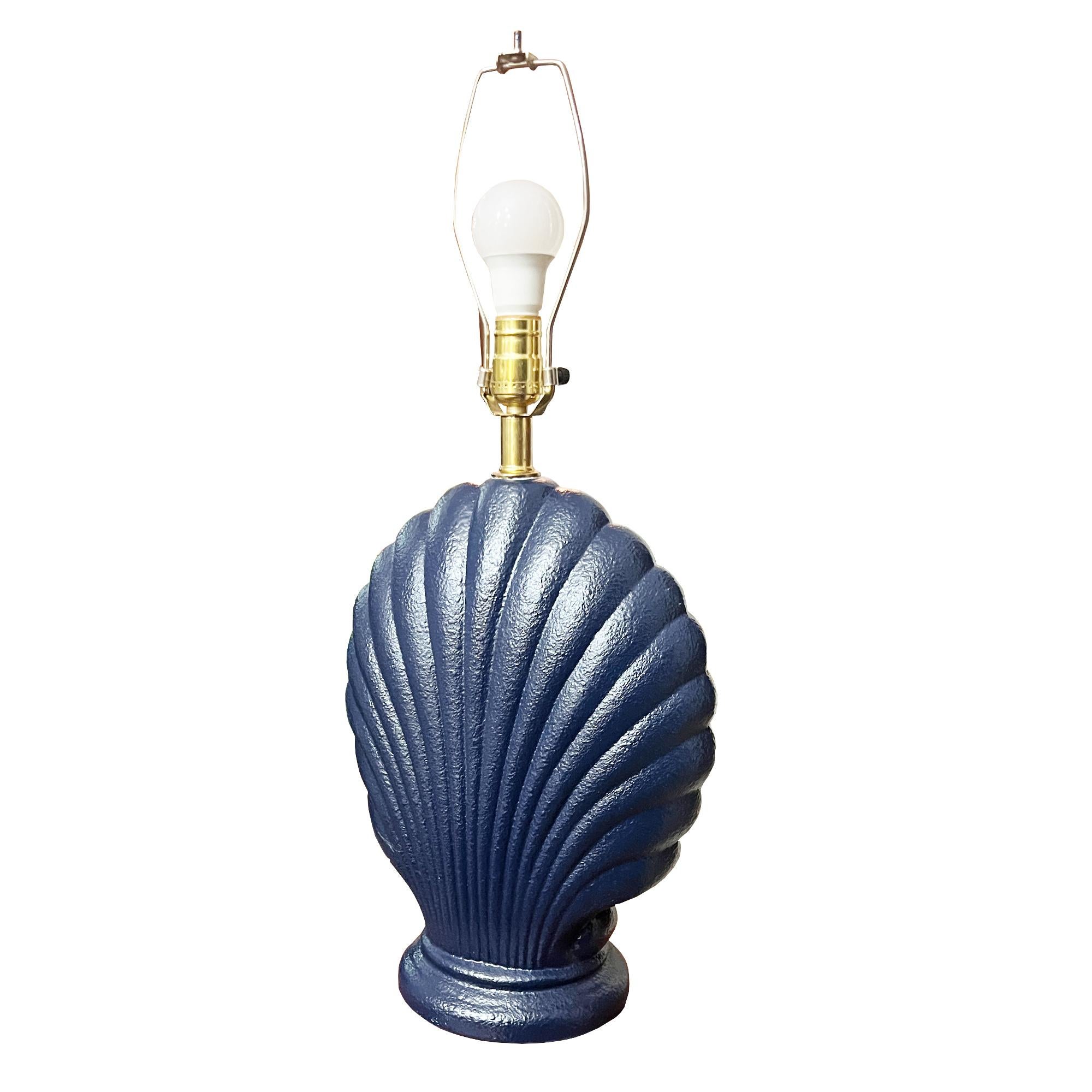A sculptural ceramic plaster or ceramic seashell table lamp. It has the silhouette in deep navy with crisp fluted ridges—graphic, polished, and effortlessly coastal. The compact footprint lands perfectly on entry consoles, bedside tables, or a bar