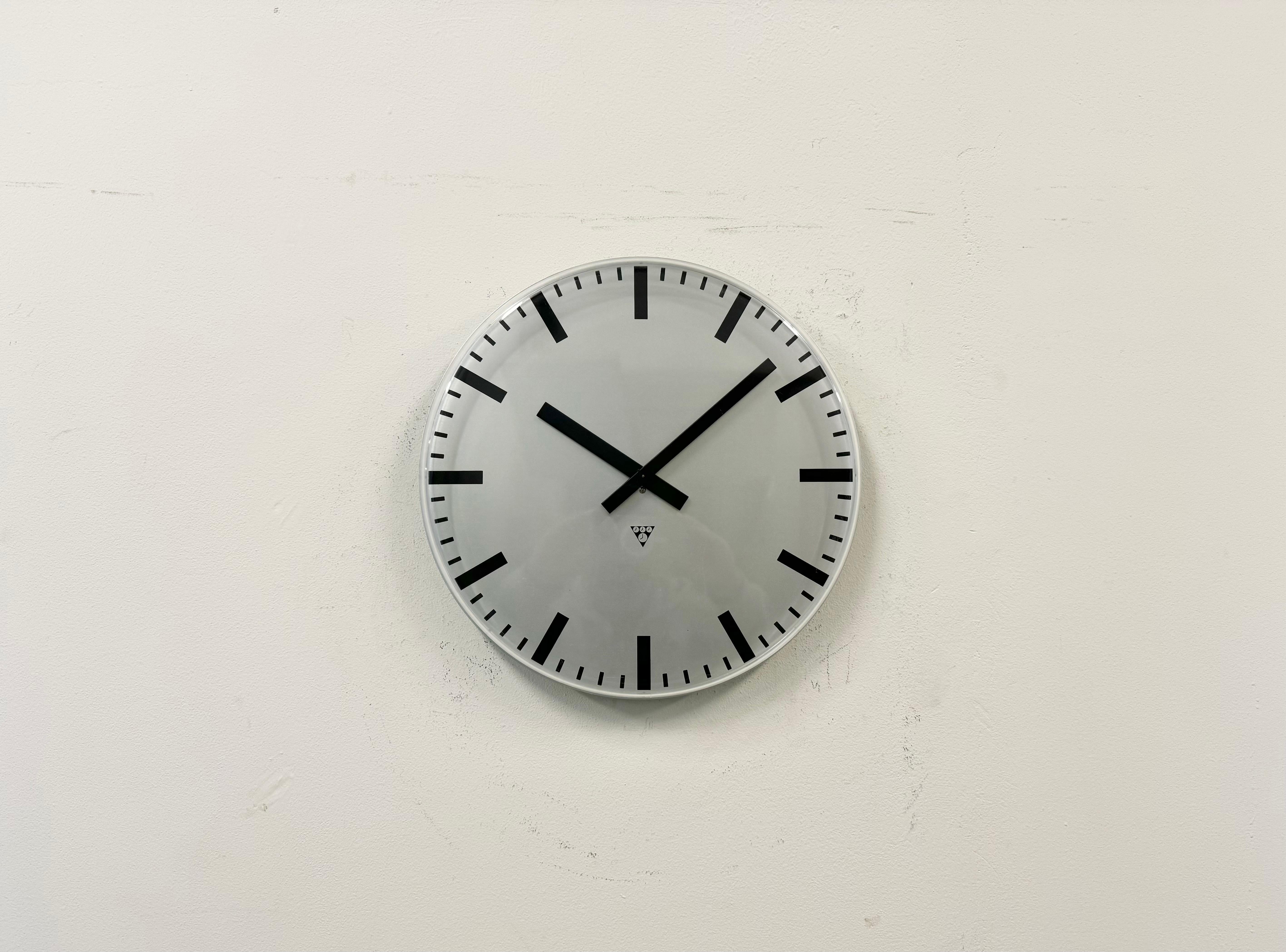 Cette horloge murale industrielle a été produite par Pragotron dans l'ancienne Tchécoslovaquie au cours des années 1980. Il est doté d'un cadran en aluminium gris (argenté) et d'un couvercle en verre transparent en plastique incurvé. La pièce a été