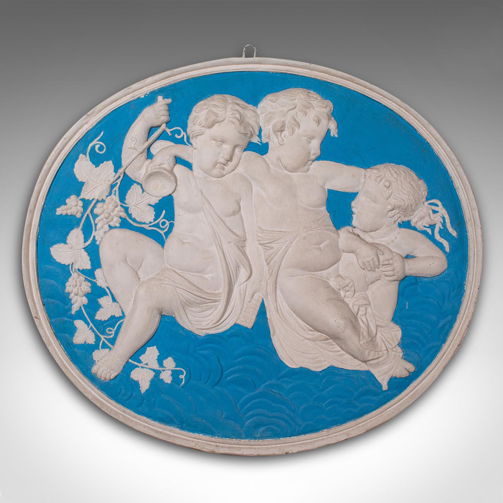 This is a vintage oval relief plaque. An English, reconstituted stone decorative frieze in the manner of Jasperware, dating to the late 20th century, circa 1980.

Wonderful putto decoration with vibrant colour, ideal for indoors or out
Displaying a