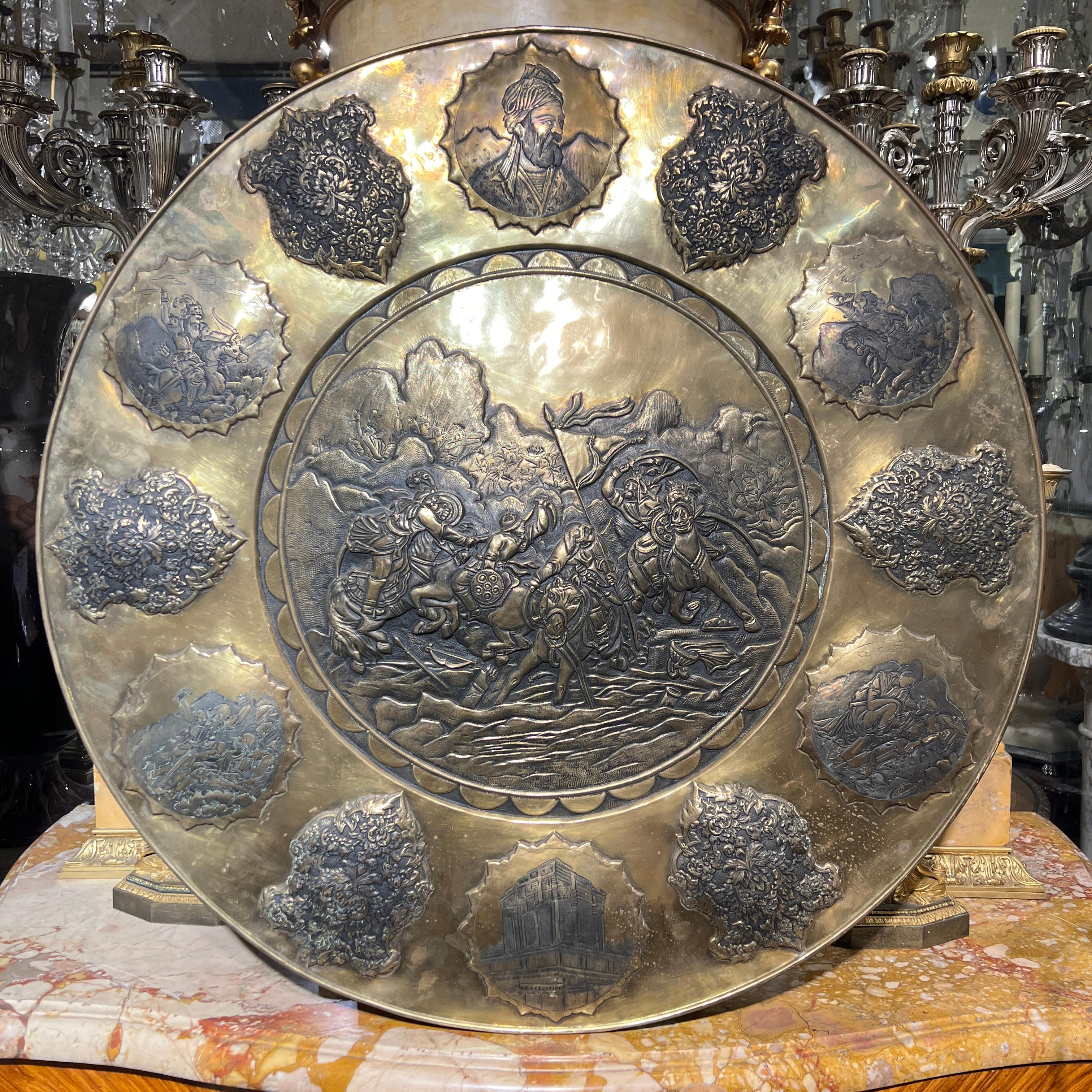 Grande caricatore d'epoca in rame in bassorilievo, di ben 30 3/4 pollici di diametro, raffigurante una drammatica battaglia tra guerrieri a cavallo in repousse e delimitato da scudi decorativi e cartigli raffiguranti il busto del celebre poeta