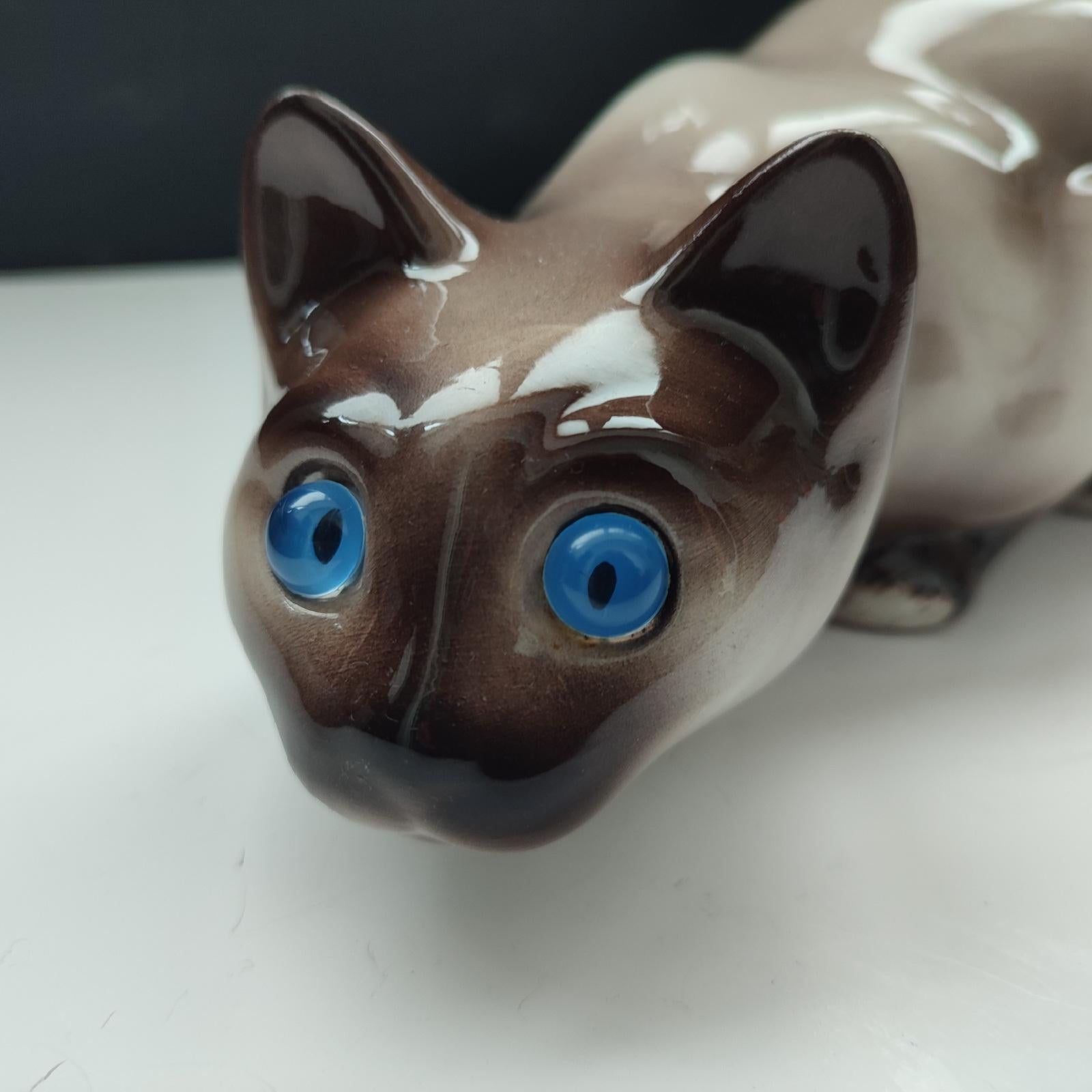 Large vintage ceramic Siamese Cat with blue glass eyes, realistic looking, ready to pounce. In excellent vintage condition with no chips or cracks. Maker's stamp on the bottom and label 'SIA' 
Dimensions: 36 cm [14.5 inch] long x 14 cm [5.5 inch]