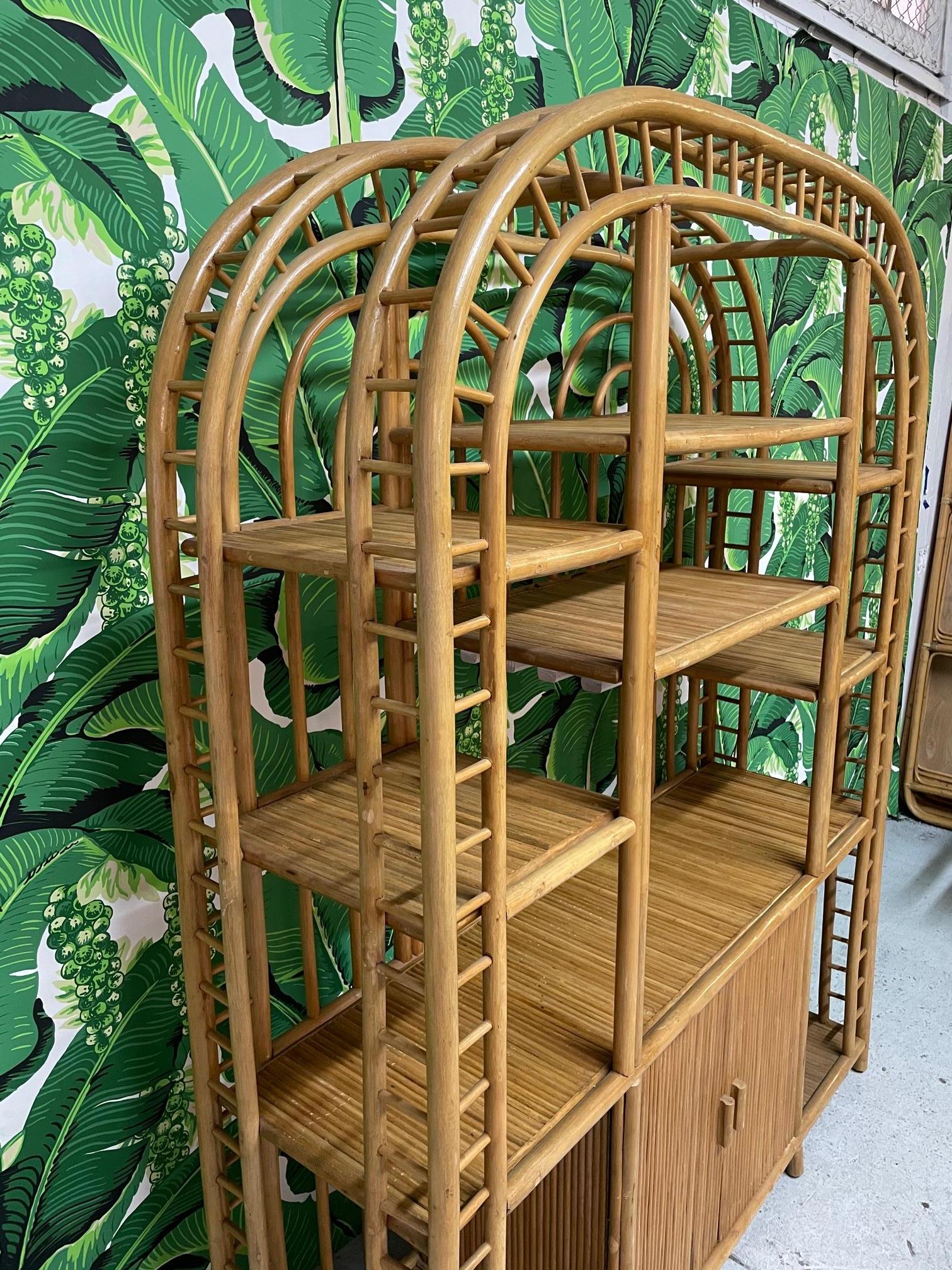 Large rattan étagère features curved top, ample shelving, and double door storage below. Interesting arch design with intricate detailing. Very good condition with minor imperfections consistent with age.