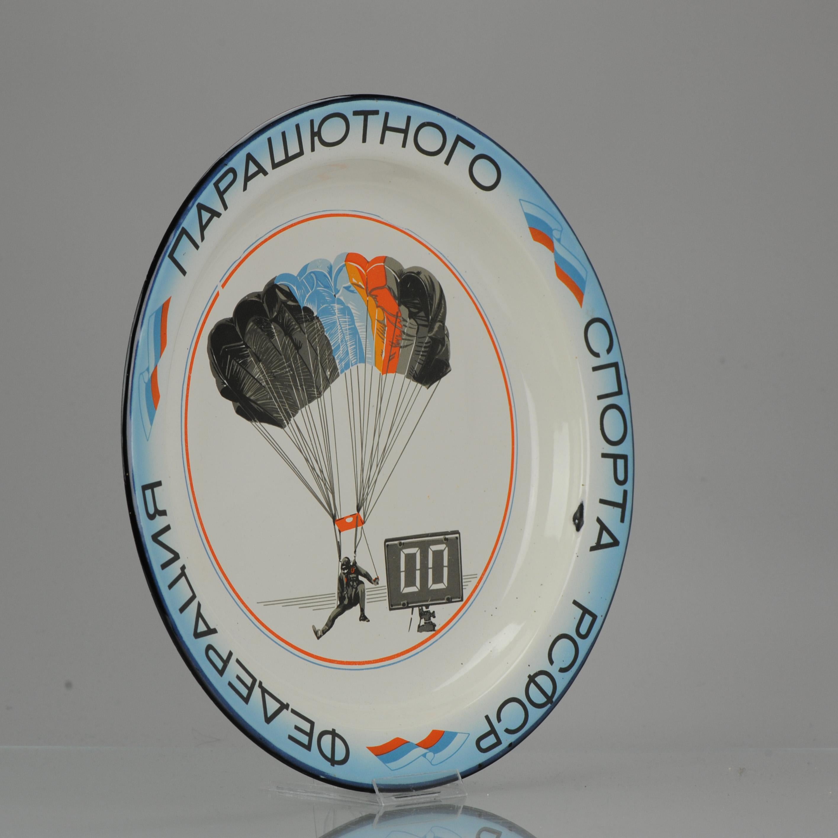 Assiette émaillée Vintage, 1991

Sur le dessus de la plaque se trouve une image d'un parachutiste, ainsi qu'une sorte d'horloge ou de compteur. Le périmètre est orné d'inscriptions russes et de drapeaux russes. Il s'agit d'une plaque commémorative