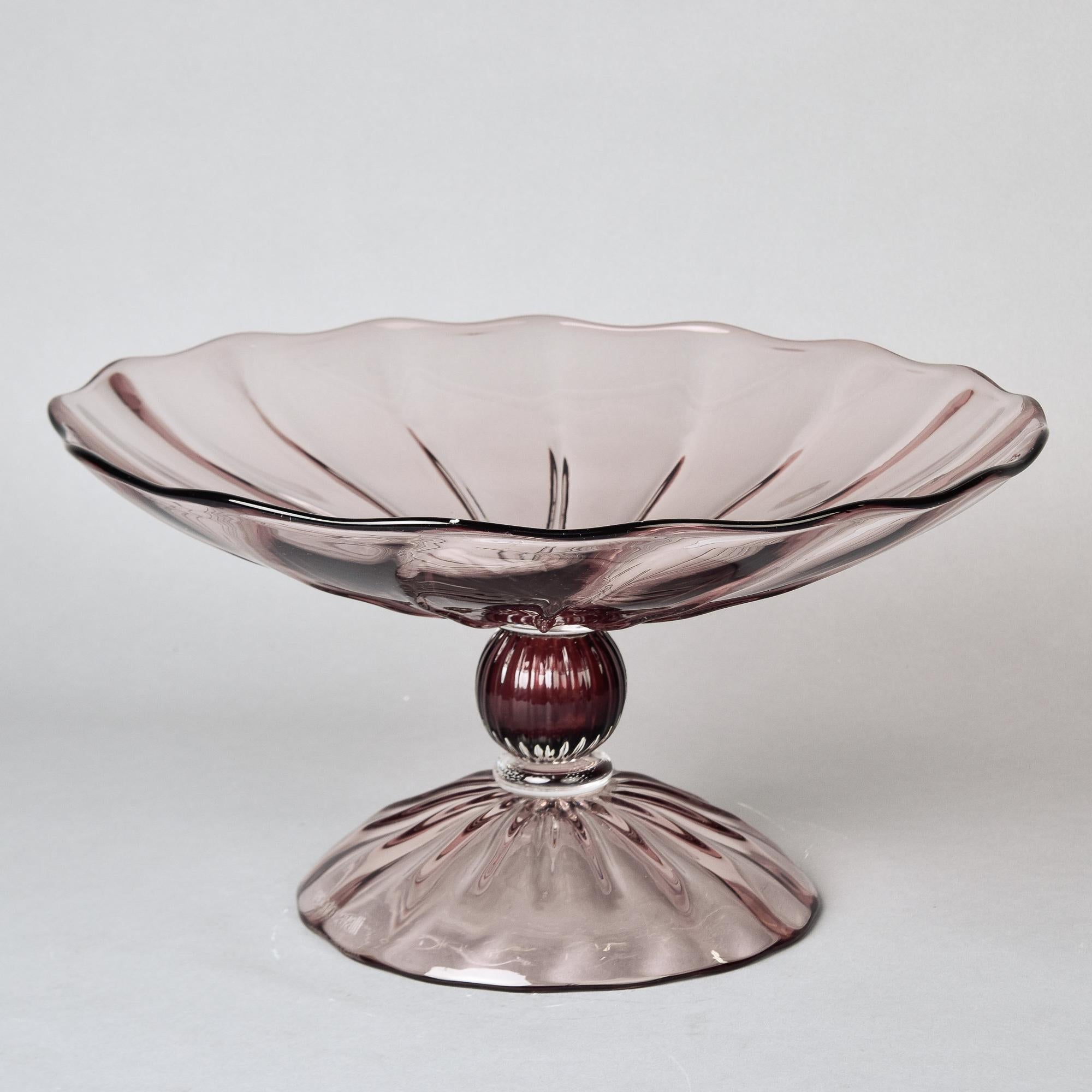 Found in Italy, this circa 2010 Murano glass tazza or pedestal bowl is marked Roberto Cavalli on the base. This pale amethyst pedestal bowl is 8.5” high and 16” diameter with subtle ribbing to the surface. No chips, cracks, flaws or repairs found.