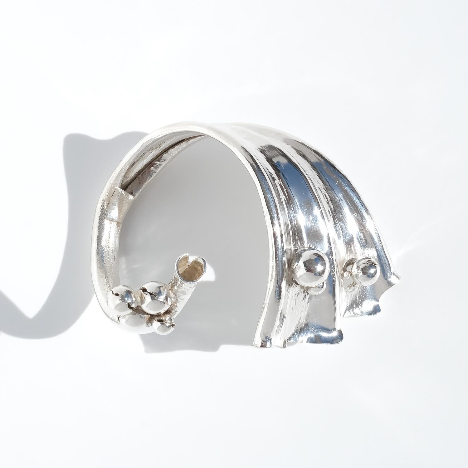 Questo massiccio e pesante bracciale vintage in argento ha una presenza audace e scultorea. La sua forma ampia e ricurva è pensata per essere indossata in alto sull'avambraccio, enfatizzando le sue dimensioni sorprendenti. La superficie strutturata,