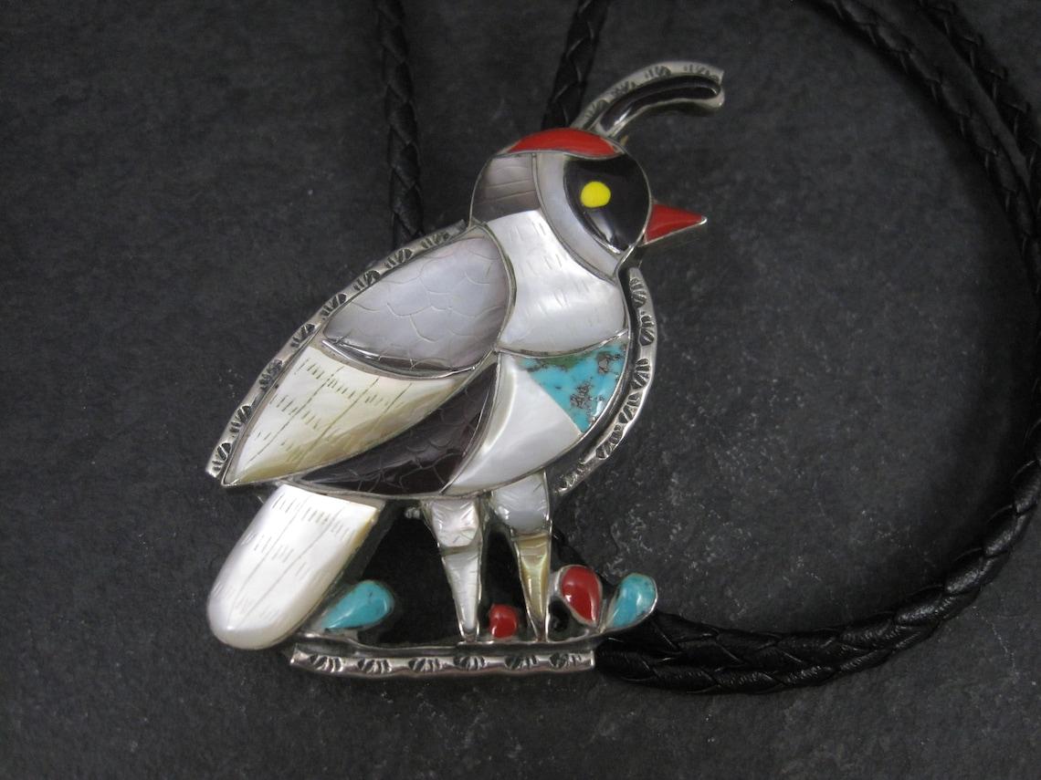 This huge, gorgeous quail bolo is sterling silver with turquoise, coral, onyx and mother of pearl inlay.

Measurements: 1 3/4 by 2 5/8 inches
Marks: Unsigned

Condition: Excellent

Included is a new 36 inch leather tie.