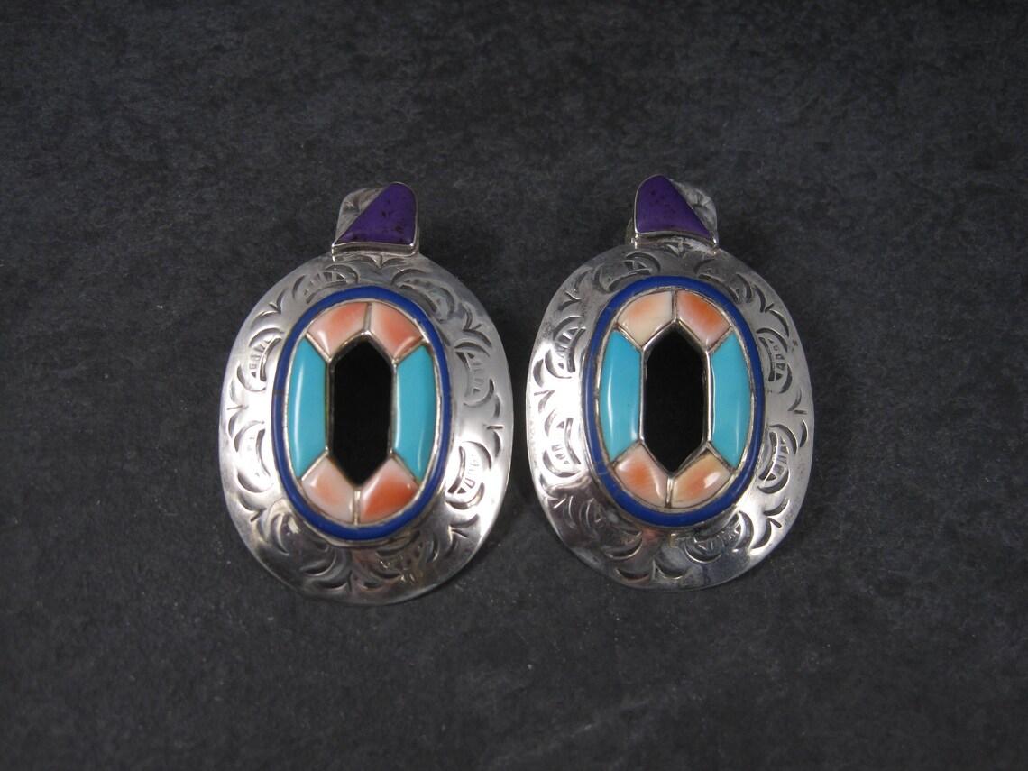 These gorgeous southwestern earrings are sterling silver.
They feature turquoise, spiny oyster and sugilite inlay.

Measurements: 1 3/8 by 2 1/16 inches
Weight: 17.3 grams

Marks: Sterling

Condition: Excellent