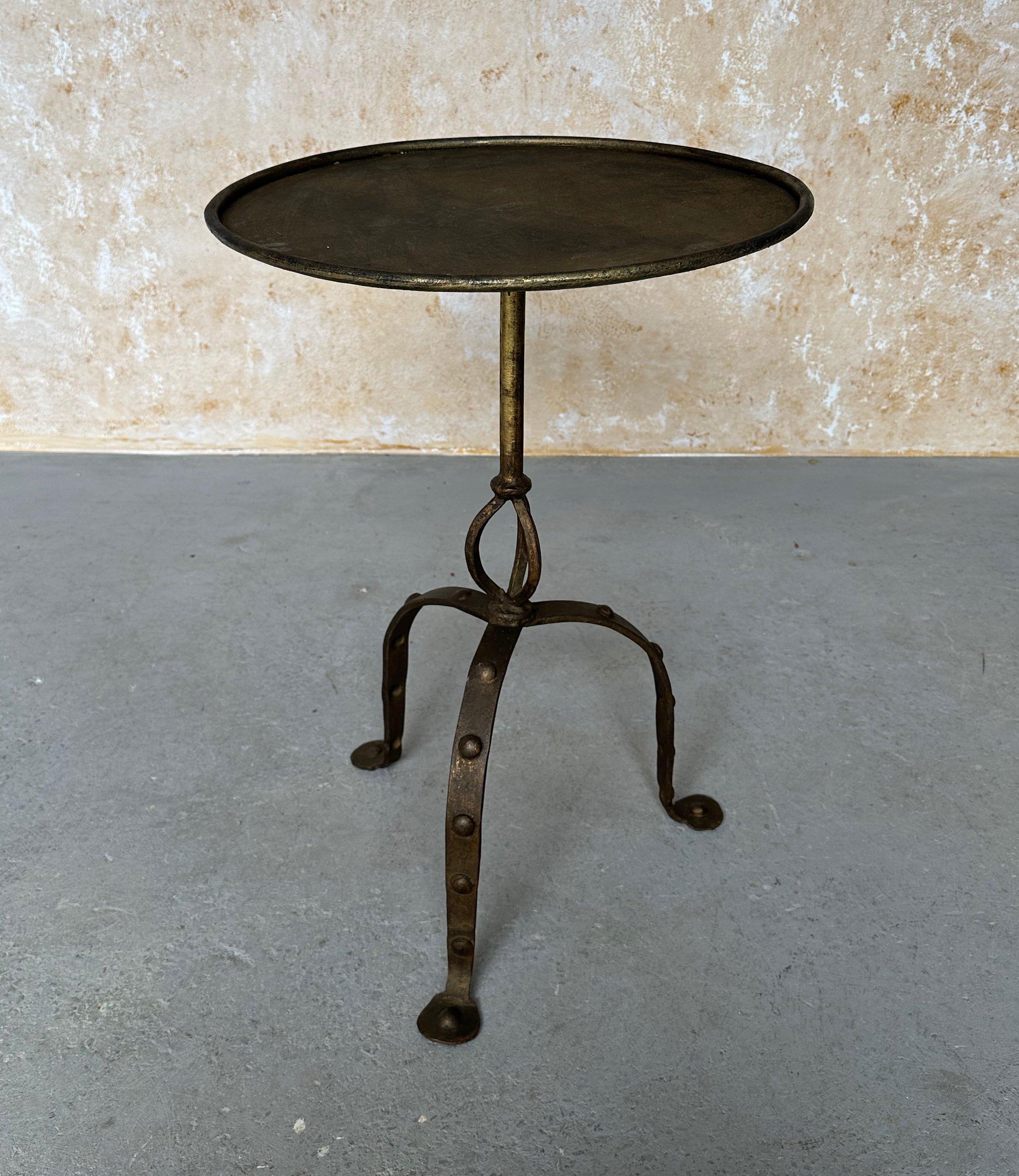 This large Spanish iron side table from the 1950s is a unique piece of vintage furniture. Measuring 26 inches in height and 18 inches in diameter, the table has a circular central stem with decorative loops at the base supported by an ornate tripod