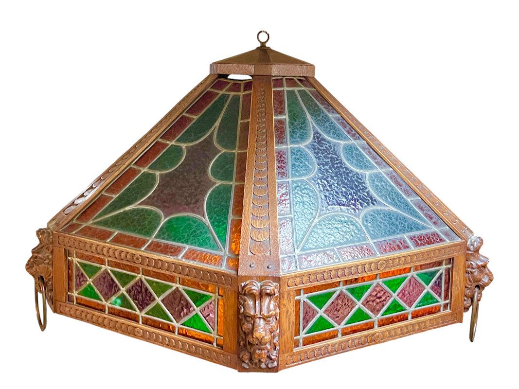 Very large vintage hexagonal shaped lantern chandelier with carved wooden frame inset with stained glass panels in green, red, violet and amber colors, featuring lion masks at the corners, with three standard sockets and wiring, ready for use.  33