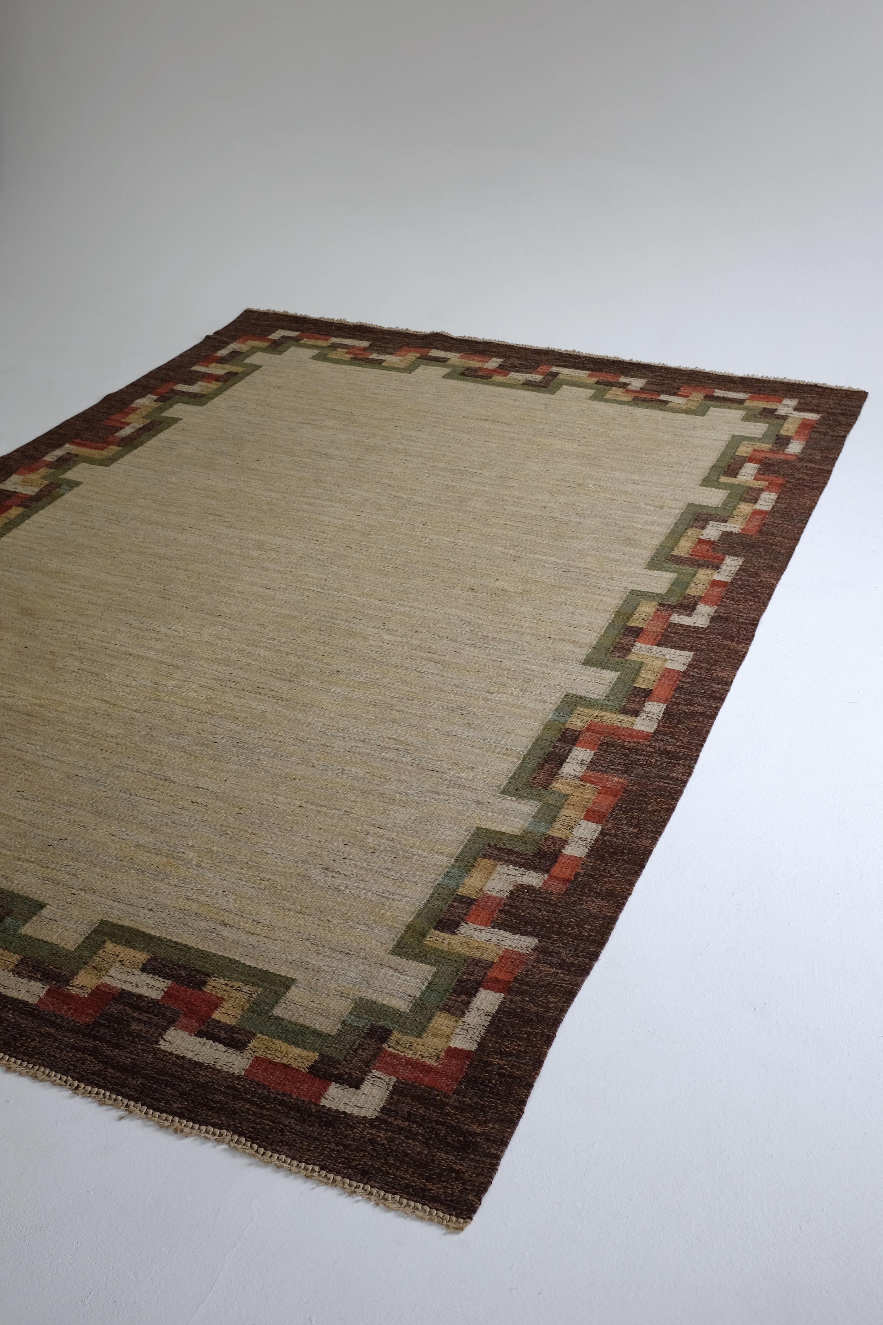 Großer schwedischer Vintage-Kilim-Teppich von unbekanntem Designer. Braune Bordüre mit grünem, weißem und rotem geometrischem Muster auf einer großen beigen Fläche in der Mitte. Die Fransen wurden gekürzt und mit leichten Gebrauchsspuren ist es in