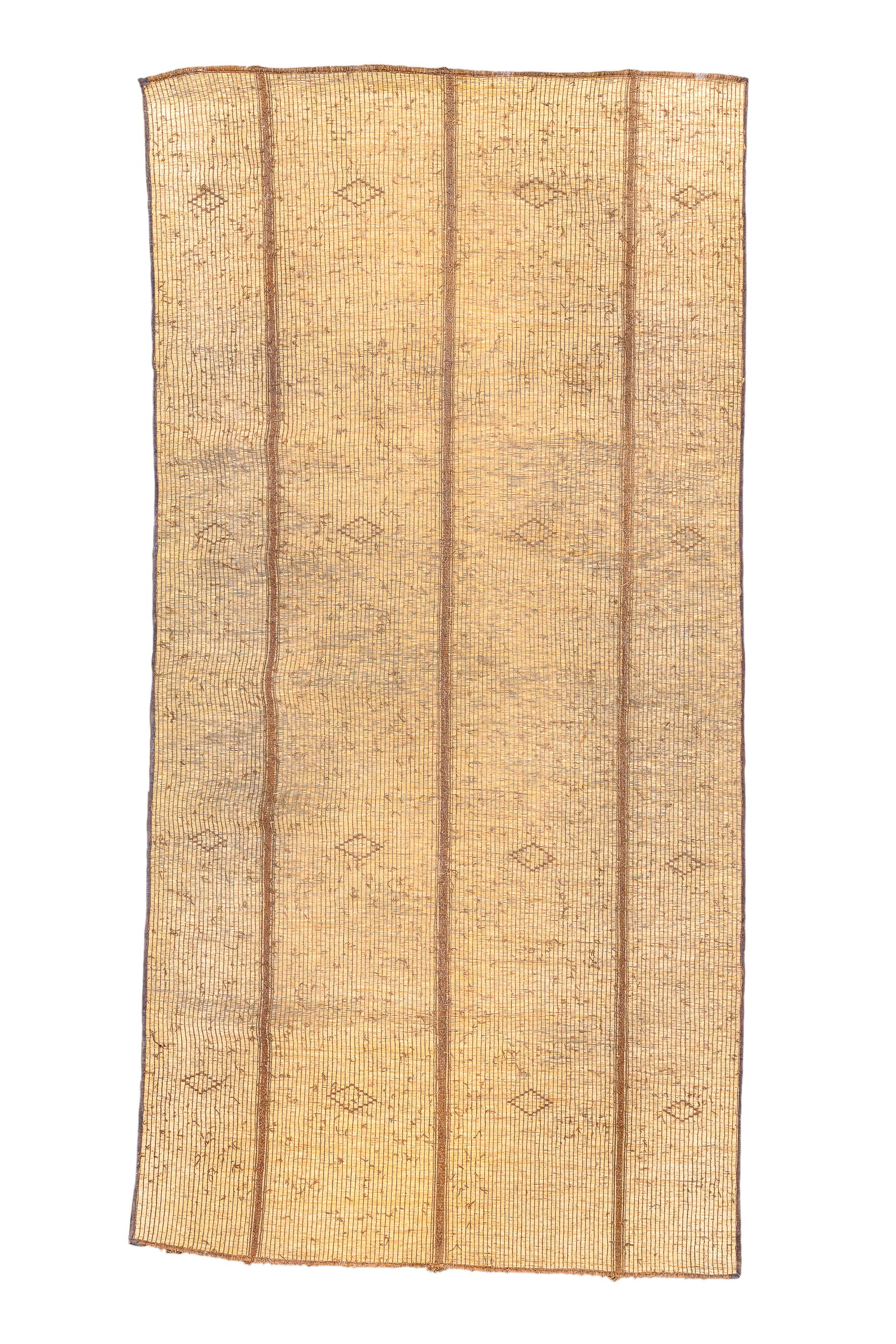 A truly flatwoven, tribal, sustainable carpet in natural tan reeds in four sections.There is a subtle pattern of small lozenges in widely spaced rows. The reeds give a flat surface with a string binding and hairline selvages. A perfect rug to was